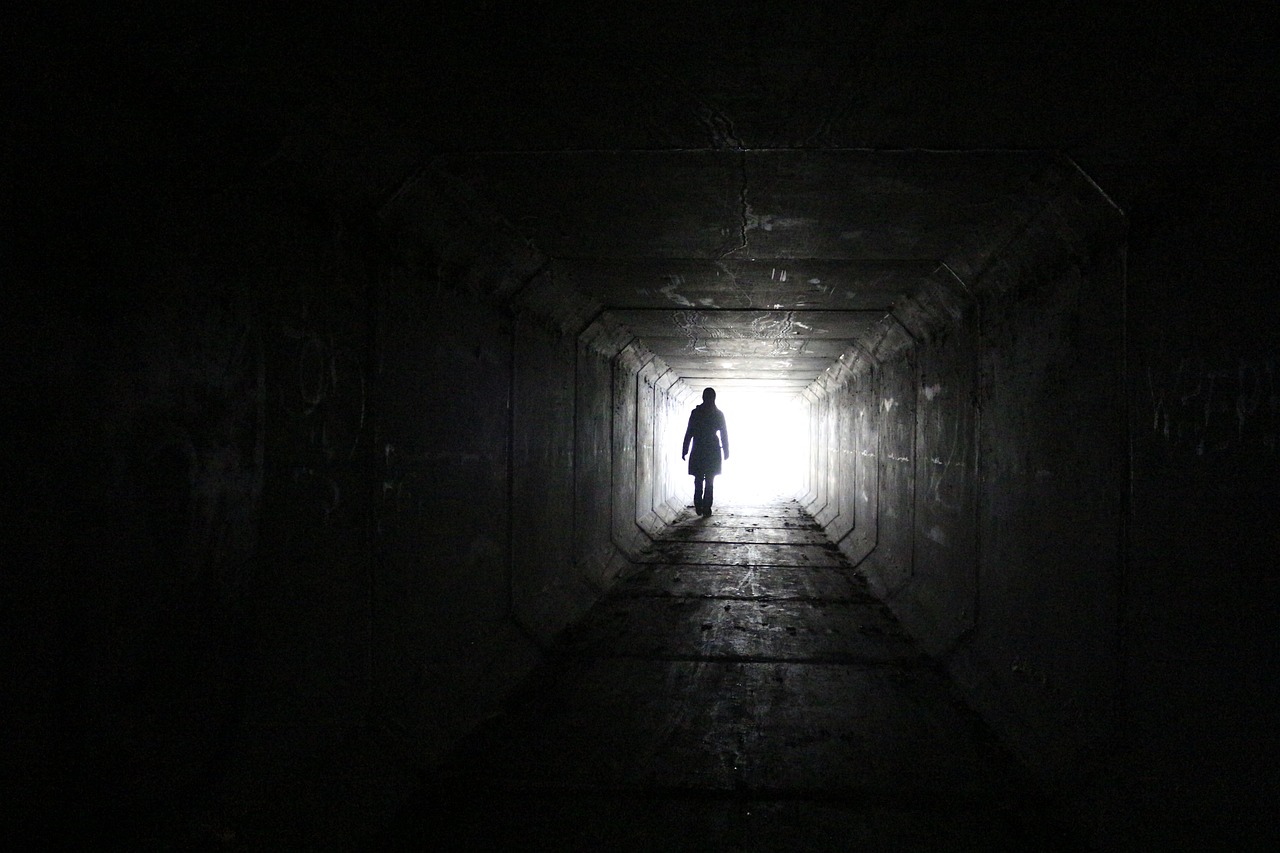 Silhouette of a person walking from a dark tunnel into a bright light