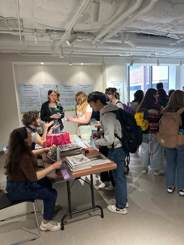 Students make newspaper pots in front of Environ 391 class posters