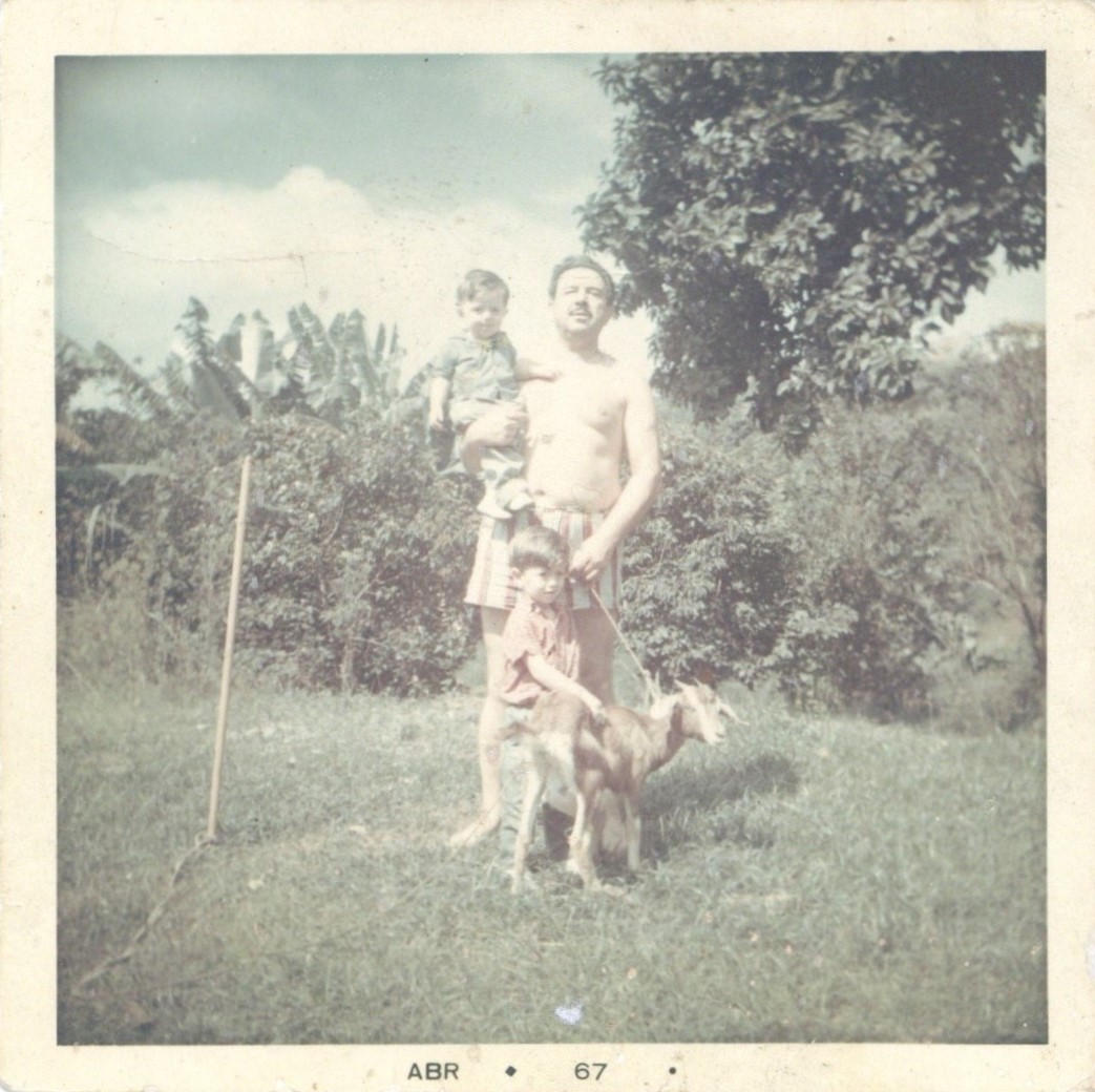 Marcelo Mirisola as a child on his grandfather's lap, his older brother standing in front of them, caressing a little goat