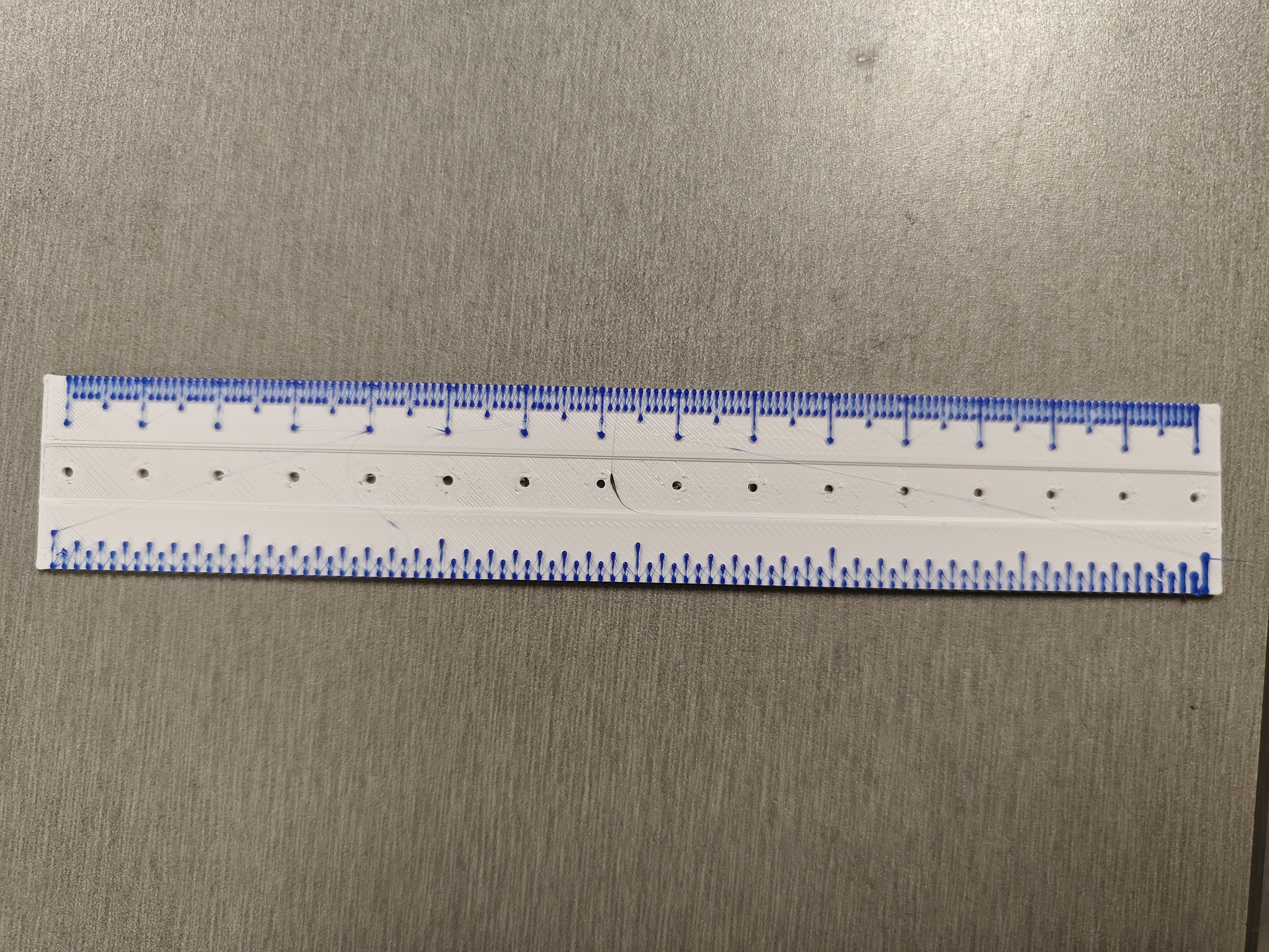 3d printed 6 inch white ruler with blue hatch marks laying on gray tabletop