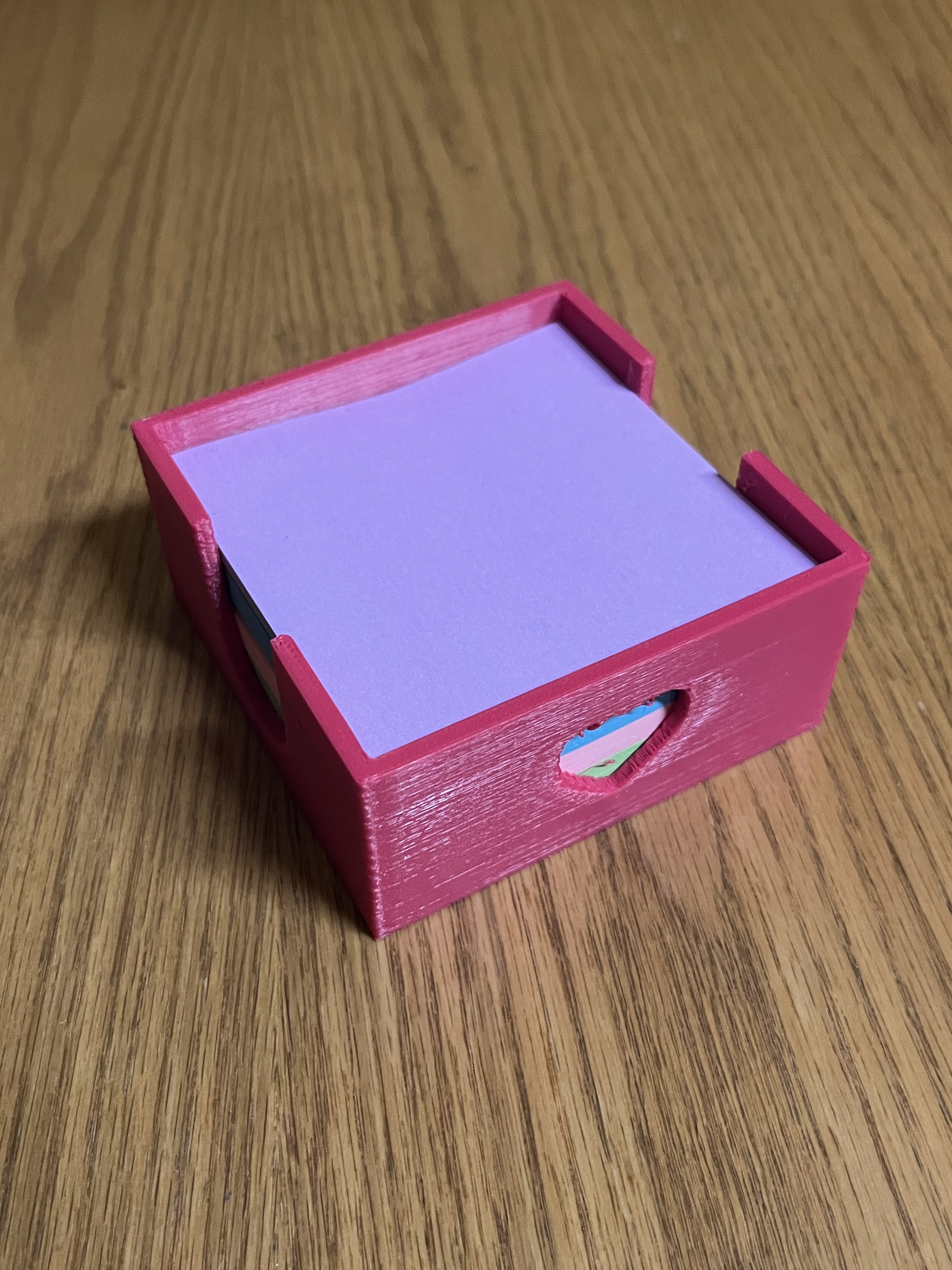 Pink 3d printed sticky note holder sitting on tabletop filled with purple sticky notes