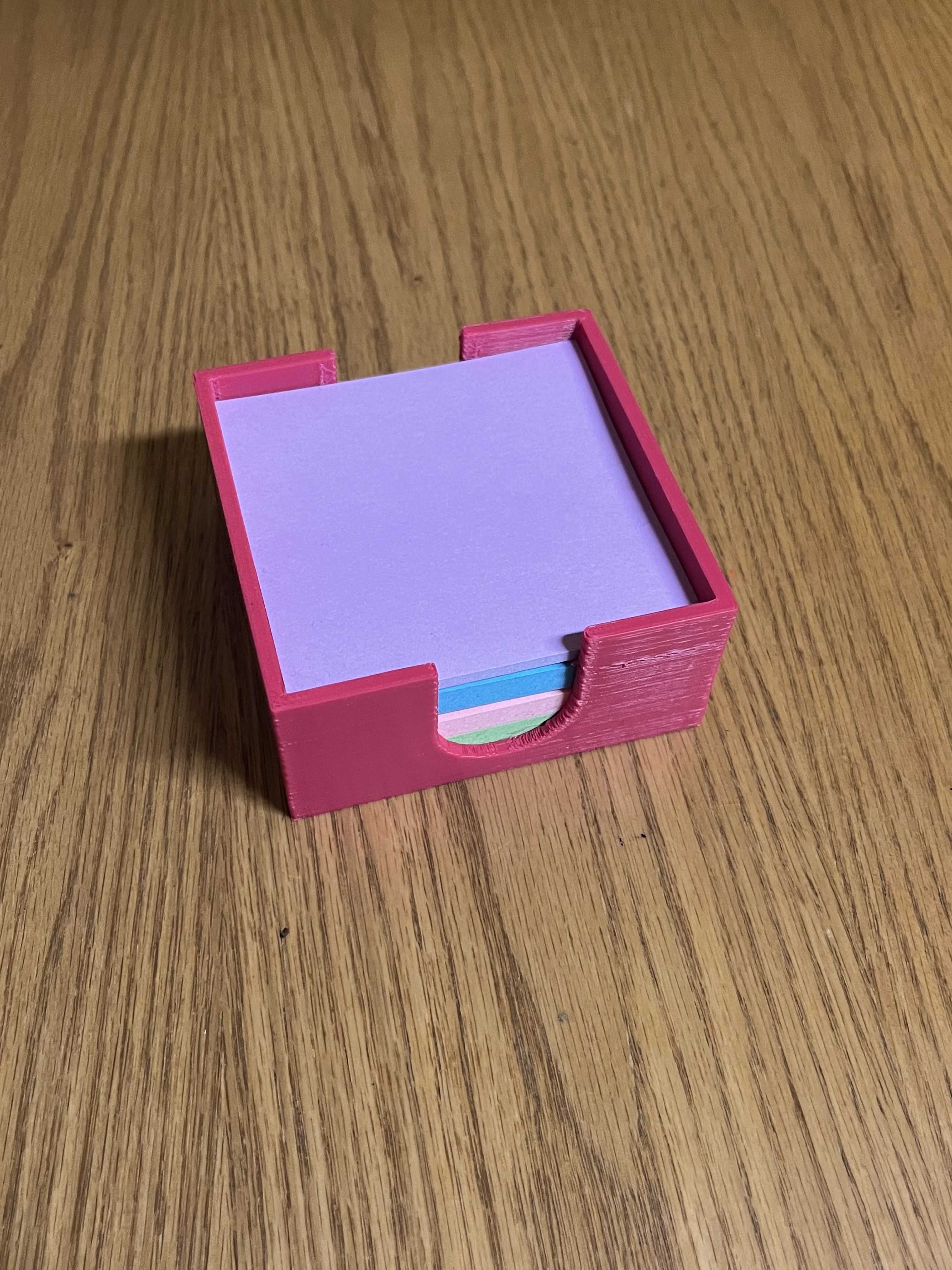 Pink 3d printed sticky note holder sitting on tabletop filled with colorful stick notpads