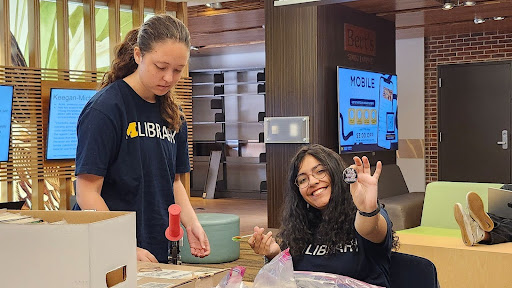 Two students in library t-shirts holding pin-back buttons.