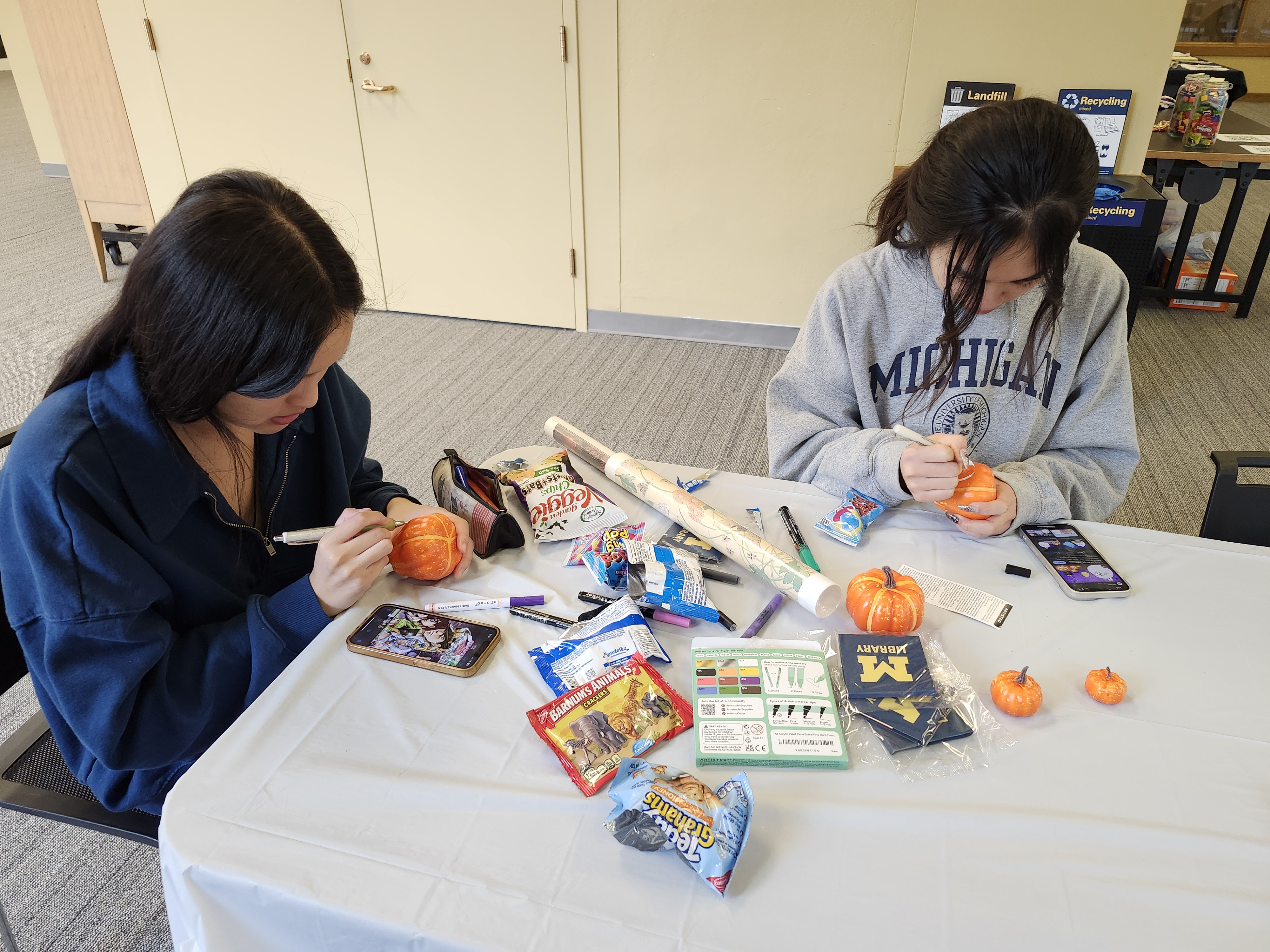 Two students decorate tiny pumpkins at a table in the Hatcher Gallery.