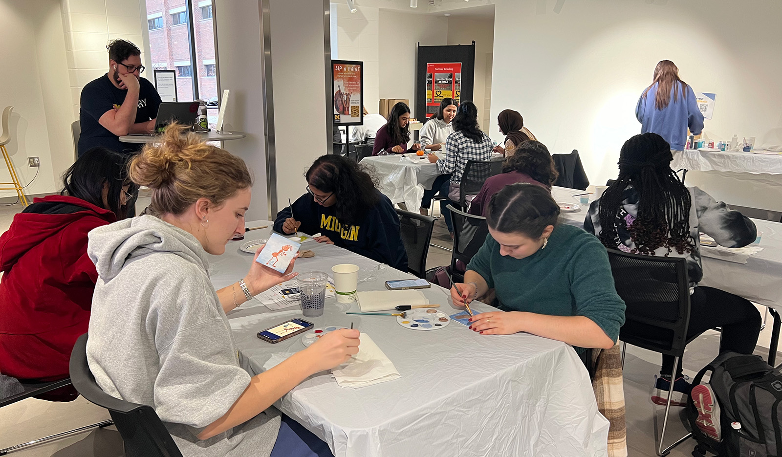 Students sit around tables painting on small canvases.