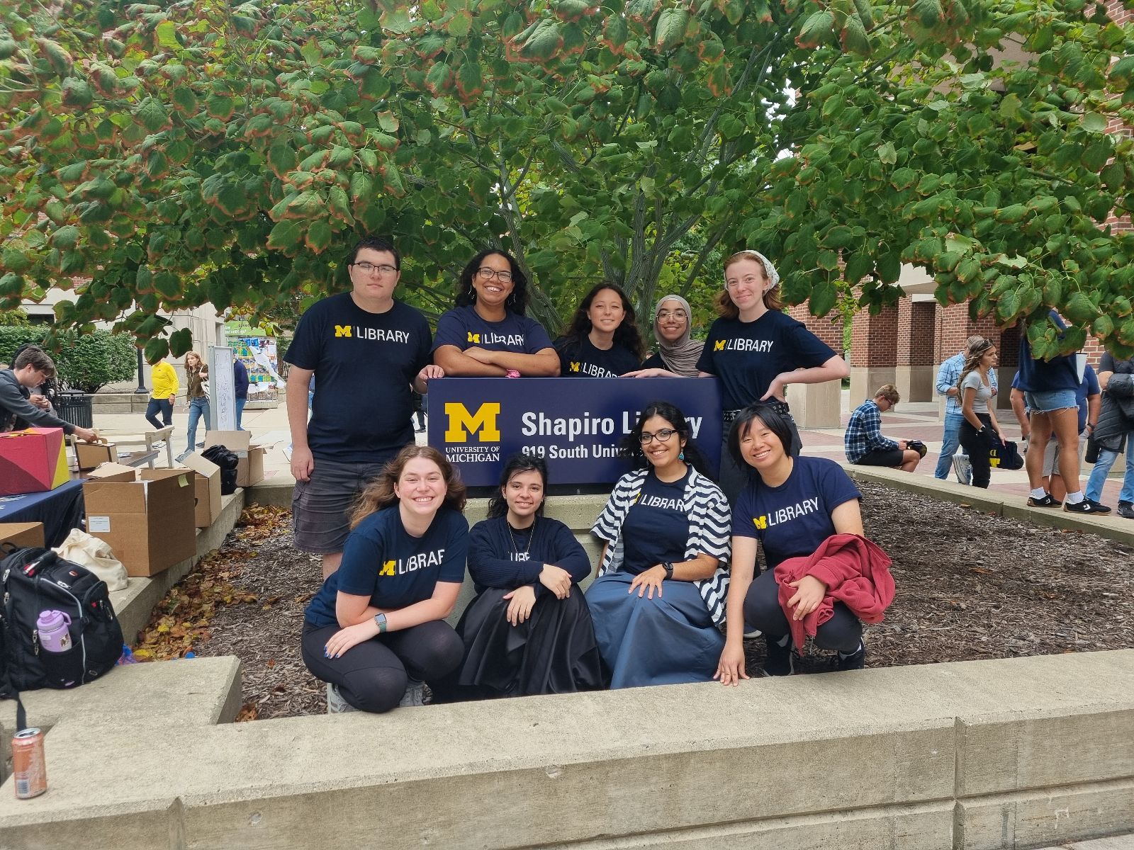 Members of the Student Library Engagement Ambassador Team (9 individuals) stand and sit around the Shapiro Library sign