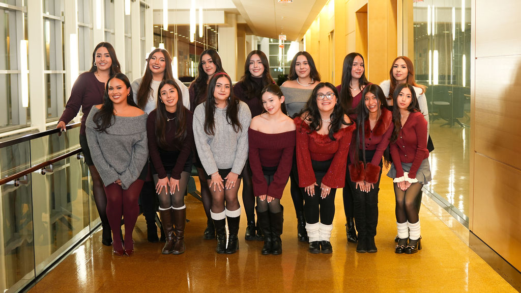 Sisters of the Lambda Theta Alpha Latin Sorority posing for a group photo. They are wearing nice casual outfits that signify their colors: grey, white, black, and dark red.