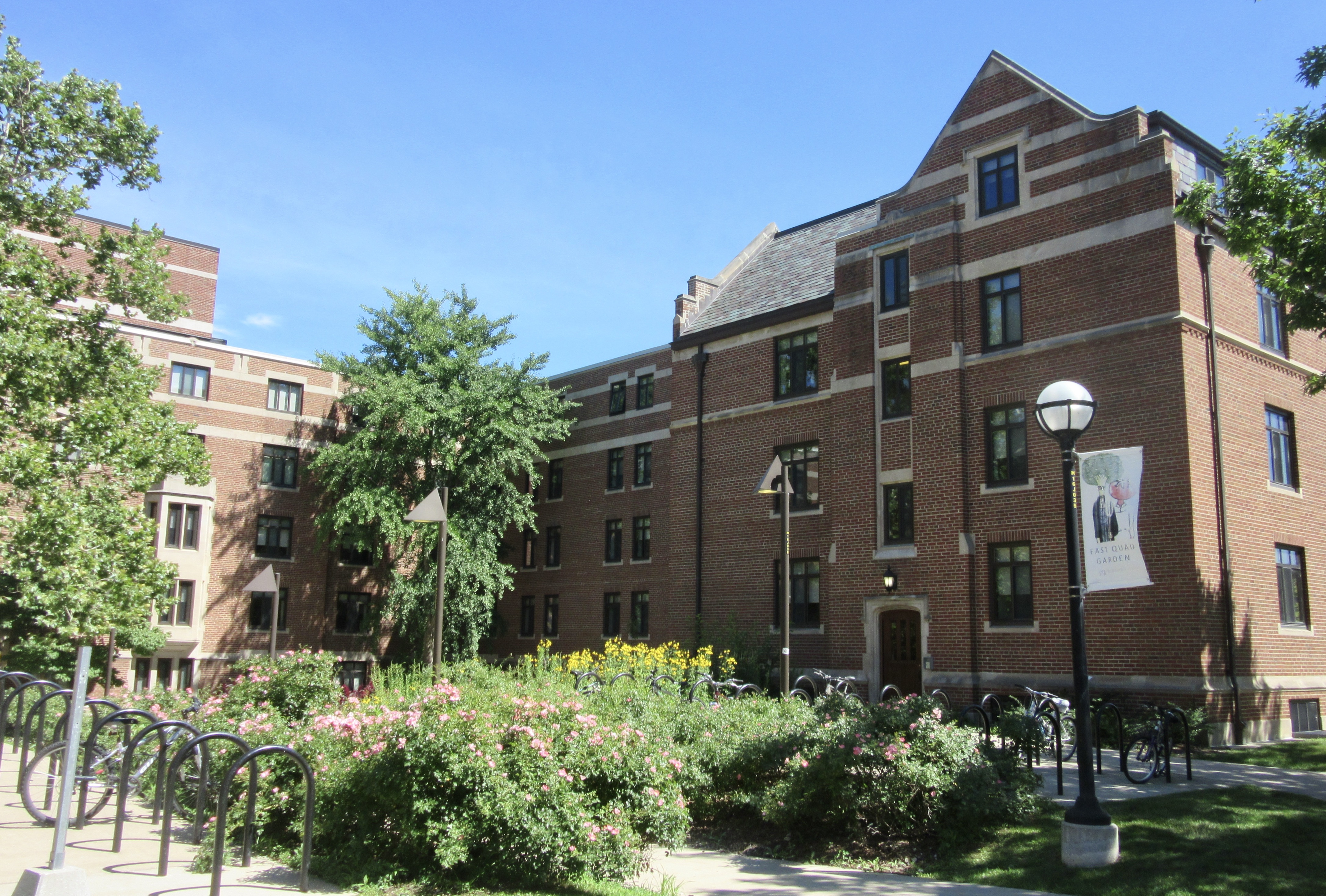 Flowering bushes and trees frame sidewalk entrance to East Quad Garden.