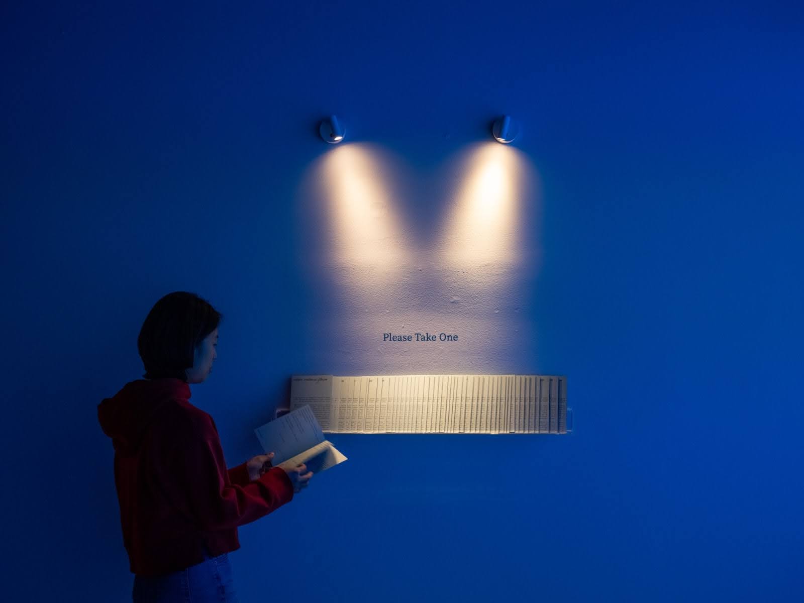 A young Asian woman looks at zines that are highlighted by spotlights in a dark room