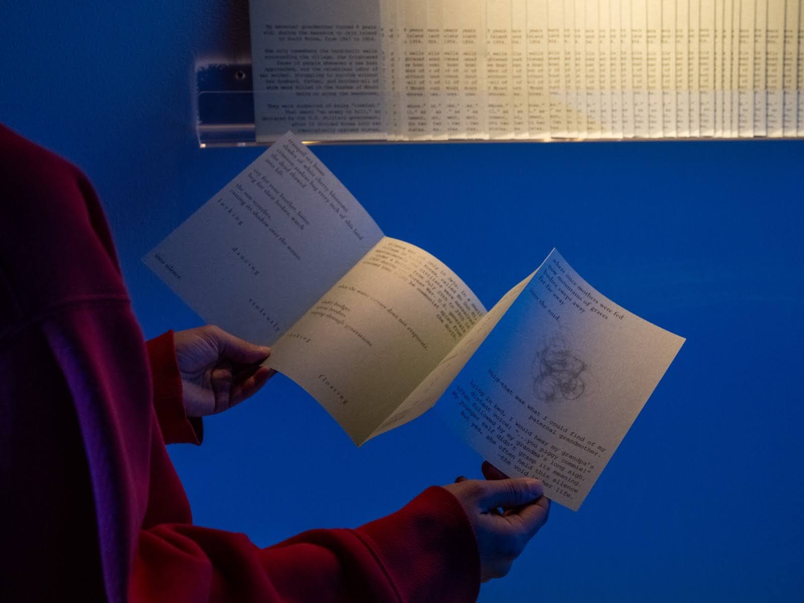 In a dark room, two hands hold up a zine to the light