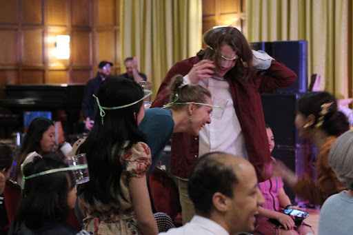 Showing a bevy of participants with strings and cups fastened around their heads as part of a cultural game called "Ping-to-the-Pong".