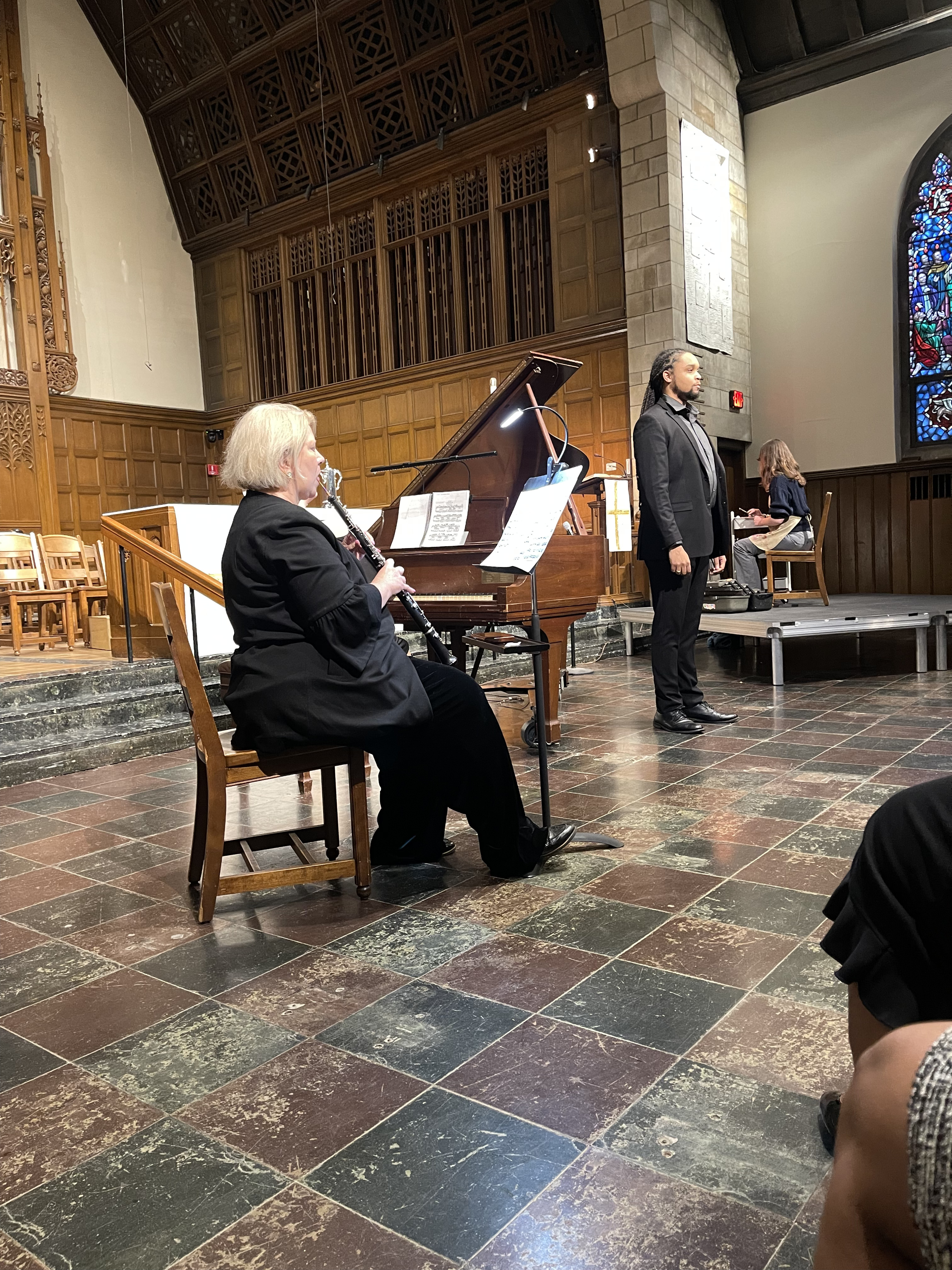 A participant in the event playing a flute-like instrument alongside another participant at the front of the room.