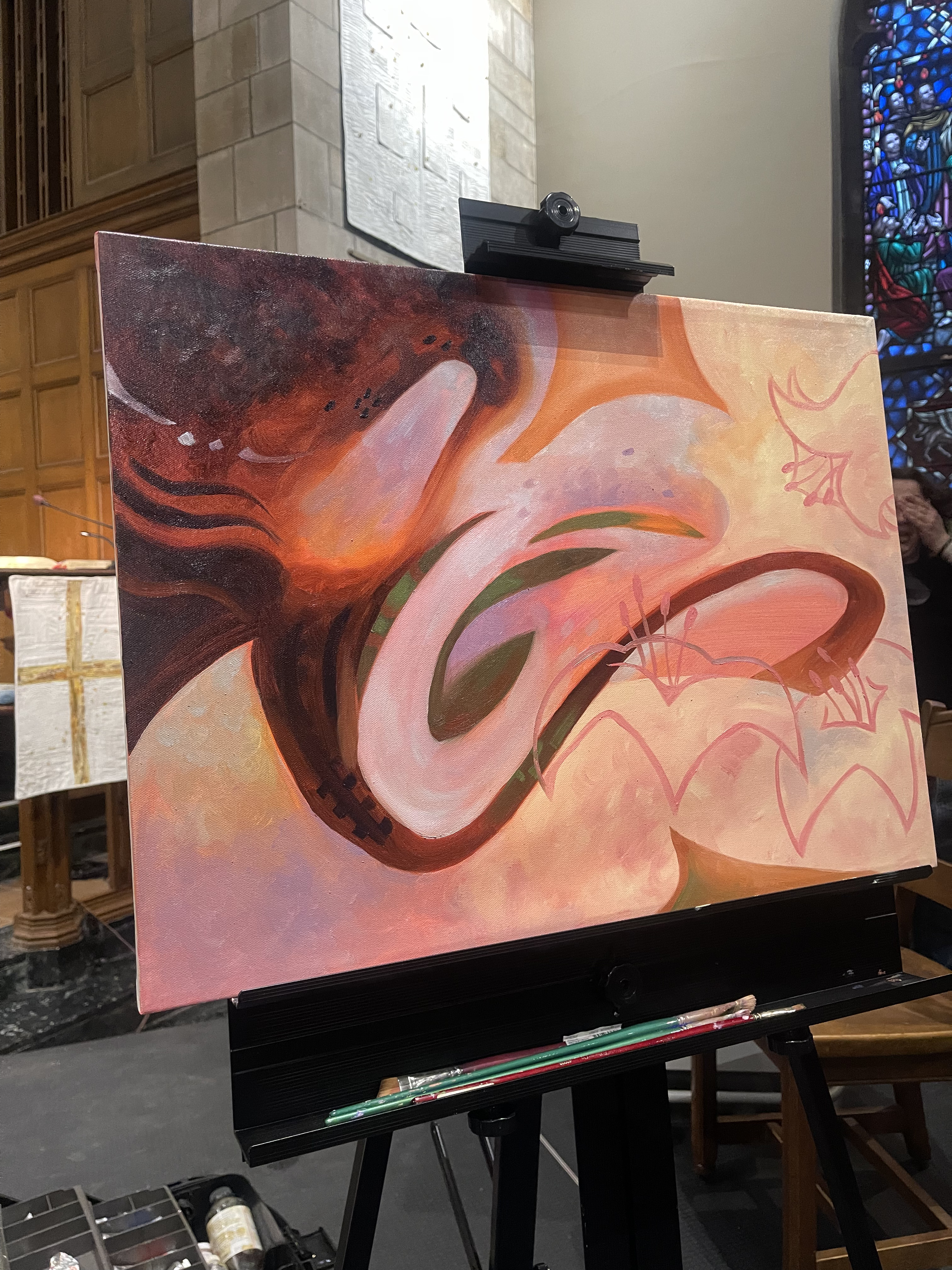 A photo depicting a piece of artwork hung on an easel stand at the event. There are bright, pastel colors and flowers in the artwork. 