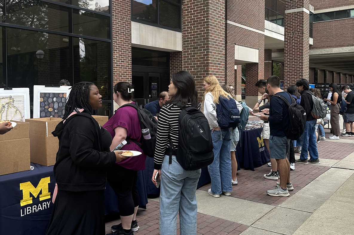 Shows a Michigan Library tabling event (Party for Your Mind) in front of Shapiro Library bustling with students and staff.