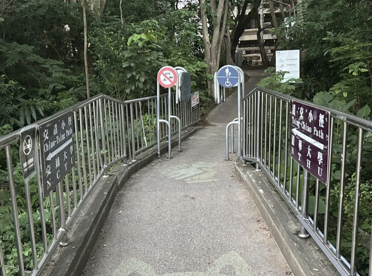 Footpath linking Yang Ming Chiao Tung University and National Tsing Hua University in Hsinchu. The sign toward Chiao Tung reads “Chiao-Tsing,” the sign toward Tsing Hua flips to “Tsing-Chiao.” A participant joked it is “one road with respective expressions (一路各表),” a campus play on the Kuomintang phrase “one China with respective interpretations (一中各表).”