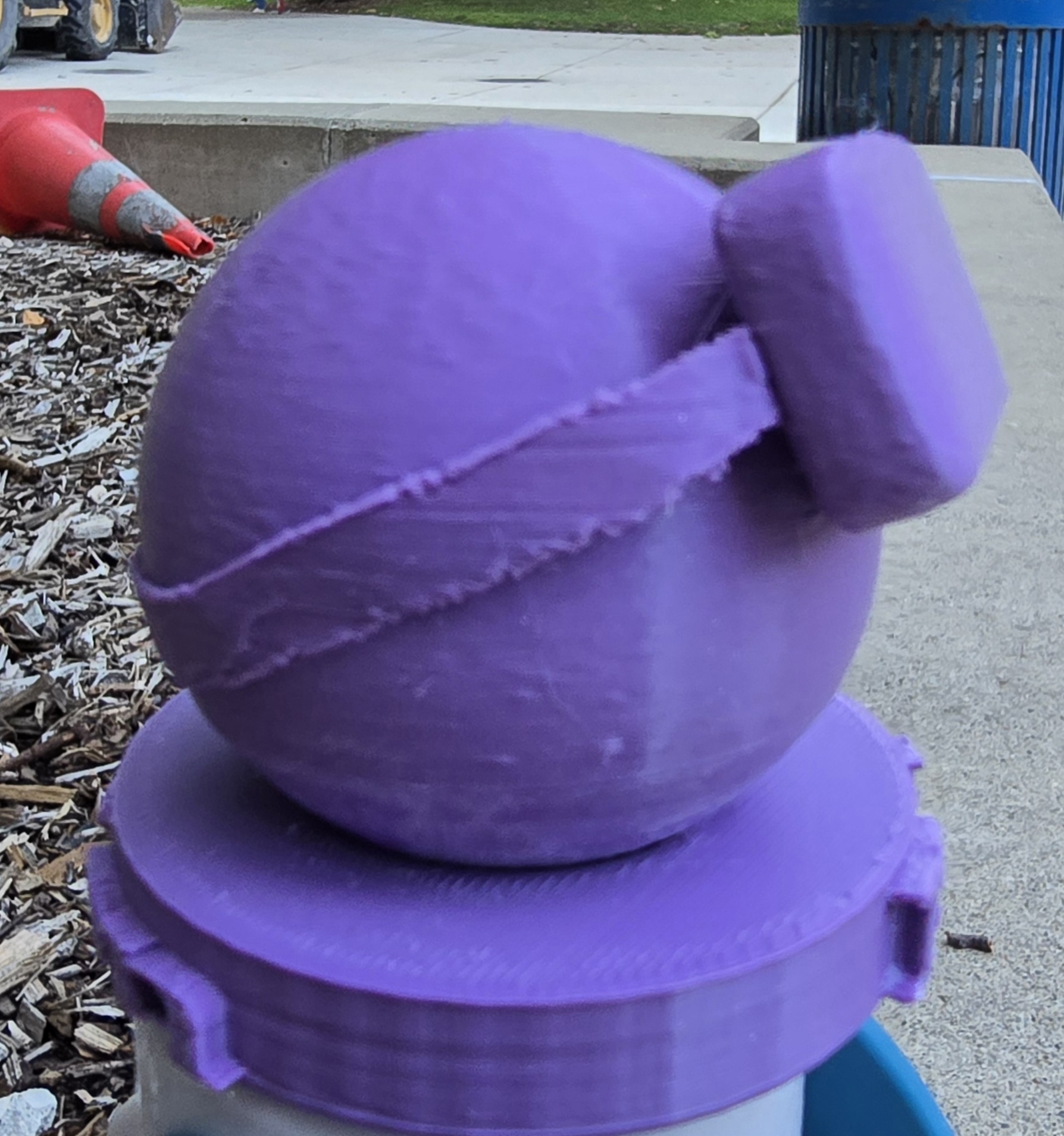 A blue, 3D printed model of a sphere wearing a pair of VR goggles on a blue stand. The picture is of the side profile of the model, with the sphere facing the right of the image.