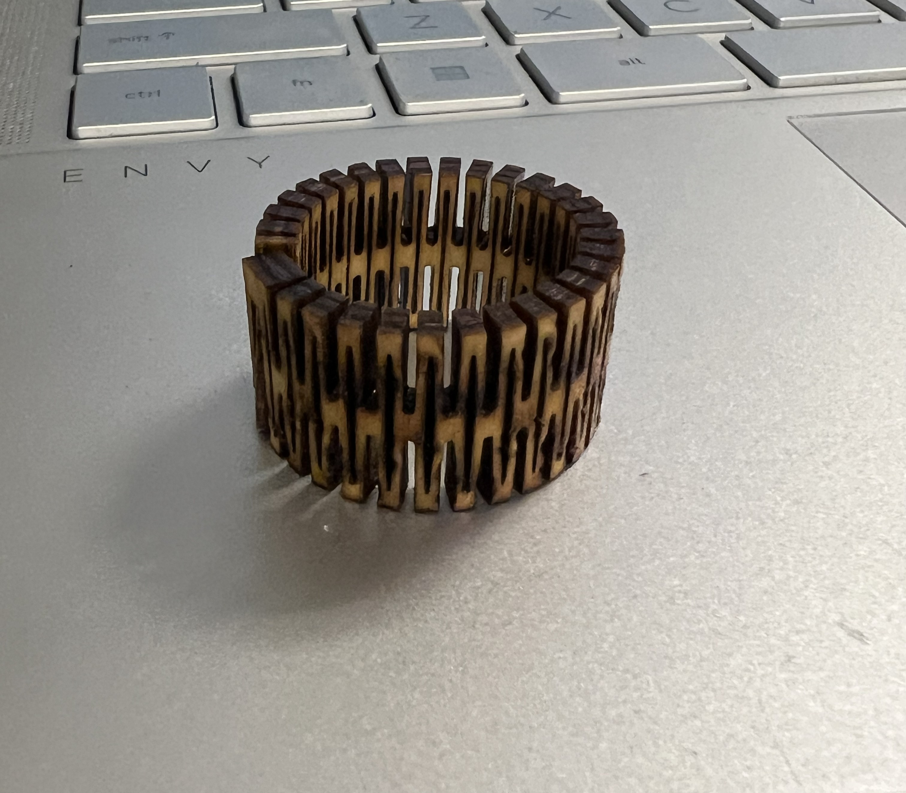 A plywood ring sitting on a laptop keyboard. The ring has a latticed texture.