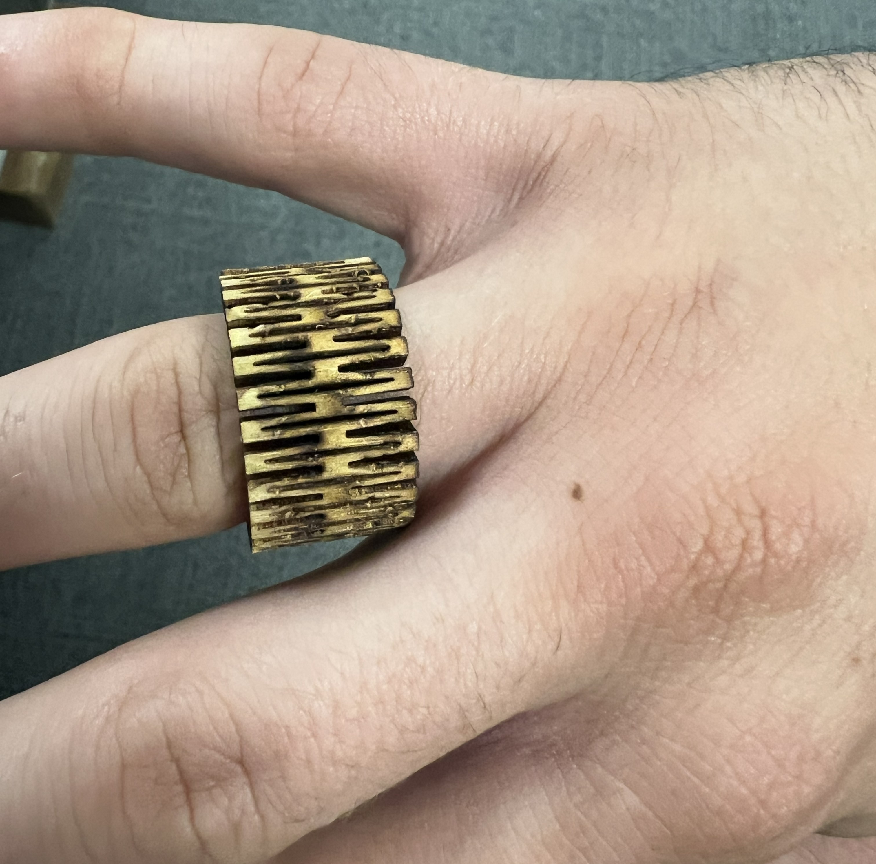 Plywood ring on a white person's ring finger. The hand is palm down, and the ring has a latticed texture.
