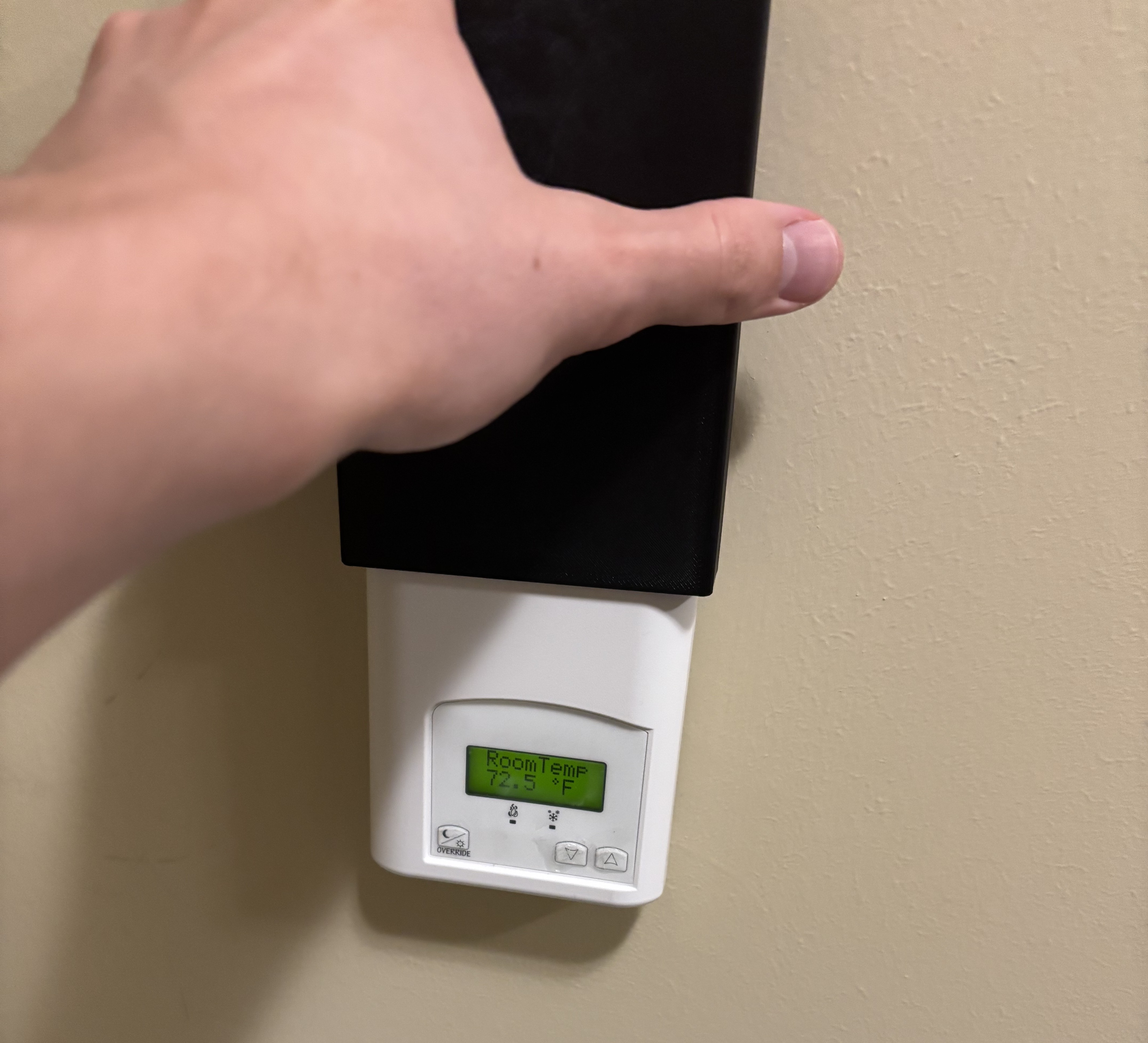 A black 3D printed sleeve being slid onto the front of the white AC control panel by a white, masculine hand. 