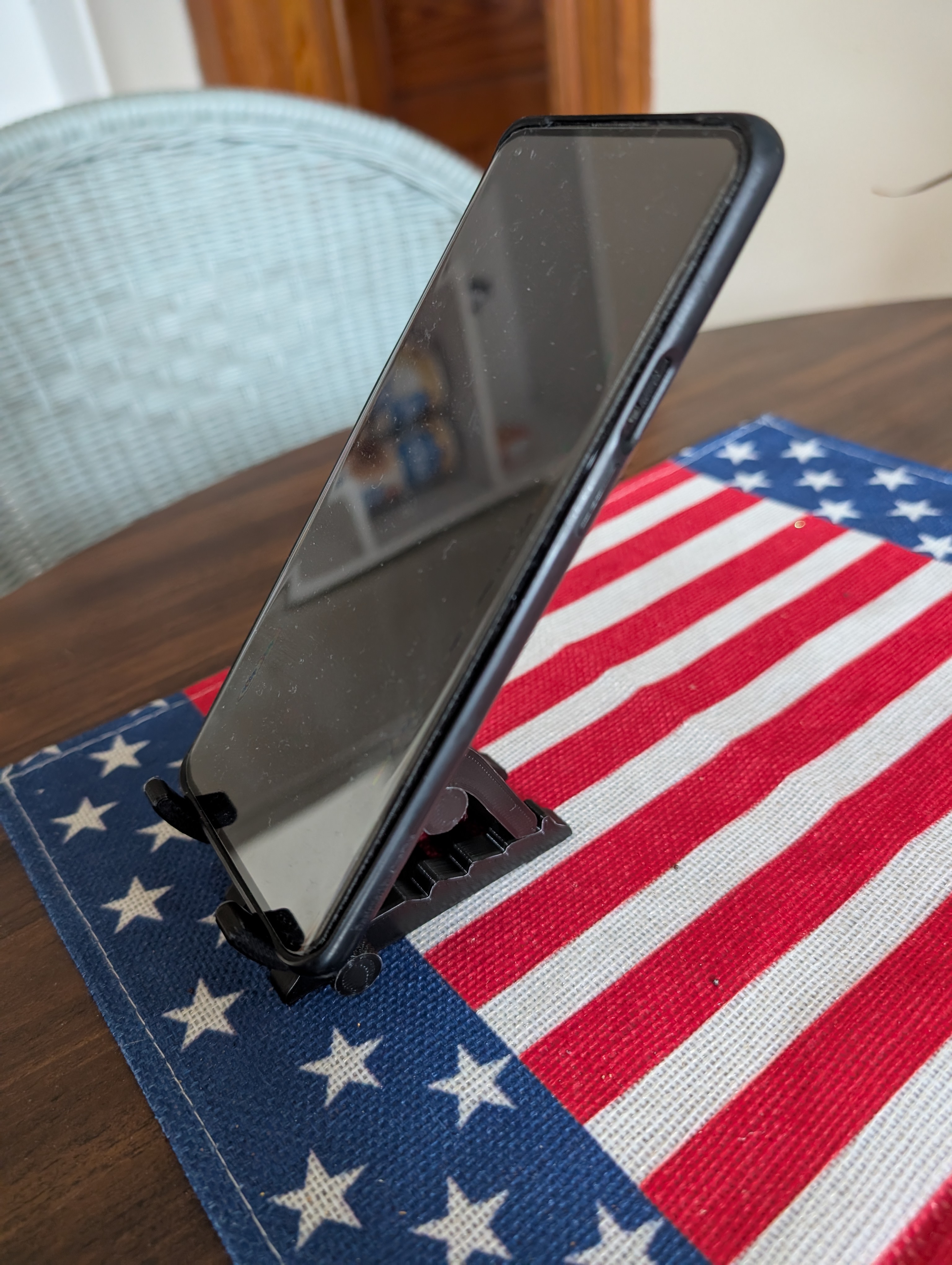 A black phone being supported by a black 3d printed phone stand on a wooden table.