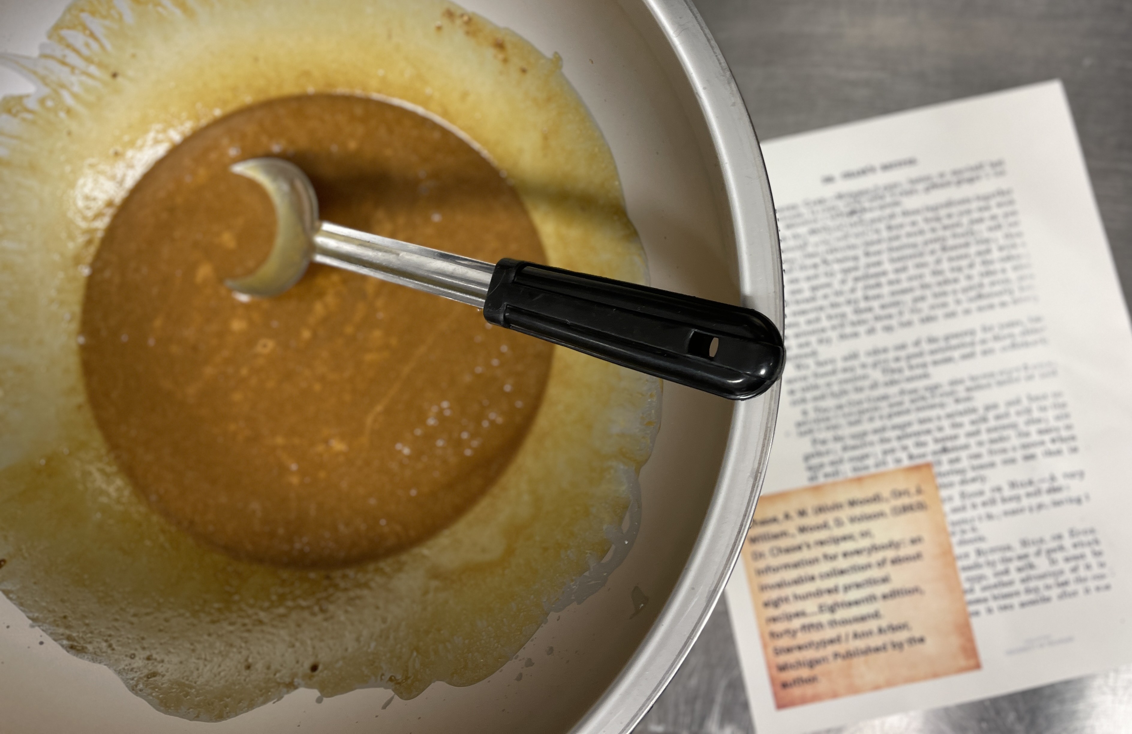 Metal bowl with brown batter in it, with a blurry recipe printout next to it