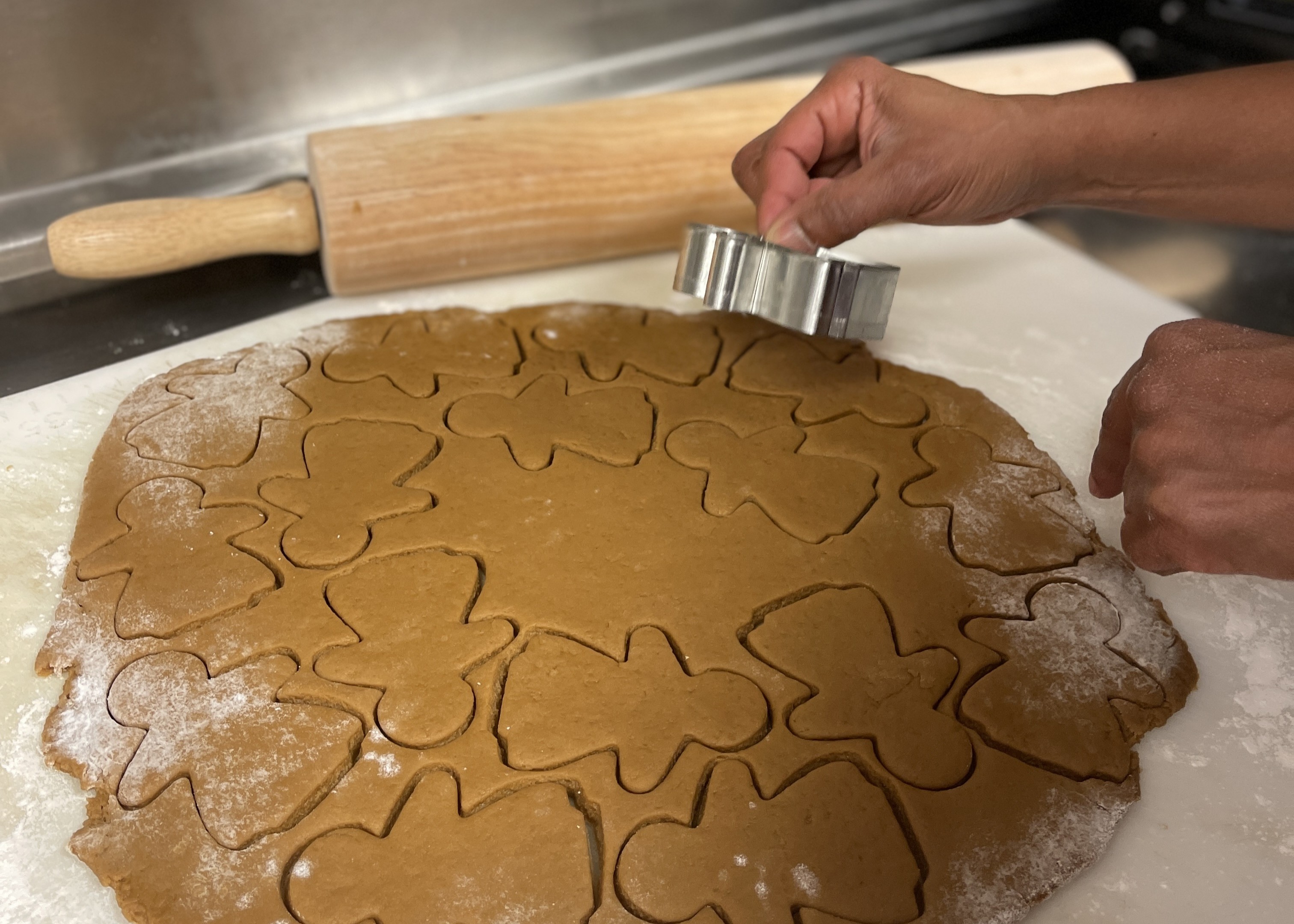 Brown cookie dough rolled flat and in the process of being cut into gingerbread women