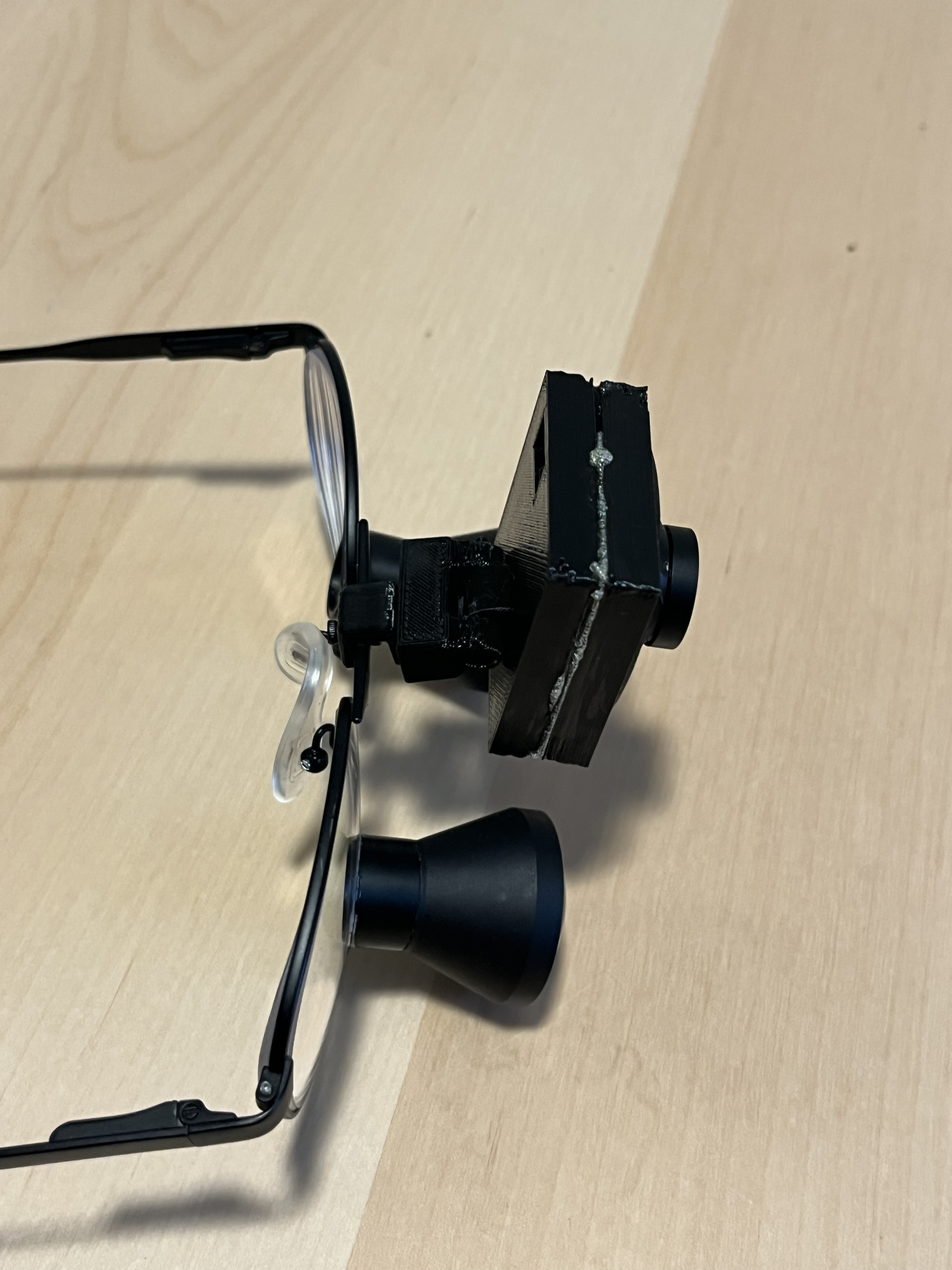 A top-down view of a 3D printed camera attached to a pair of surgical glasses with black frames..