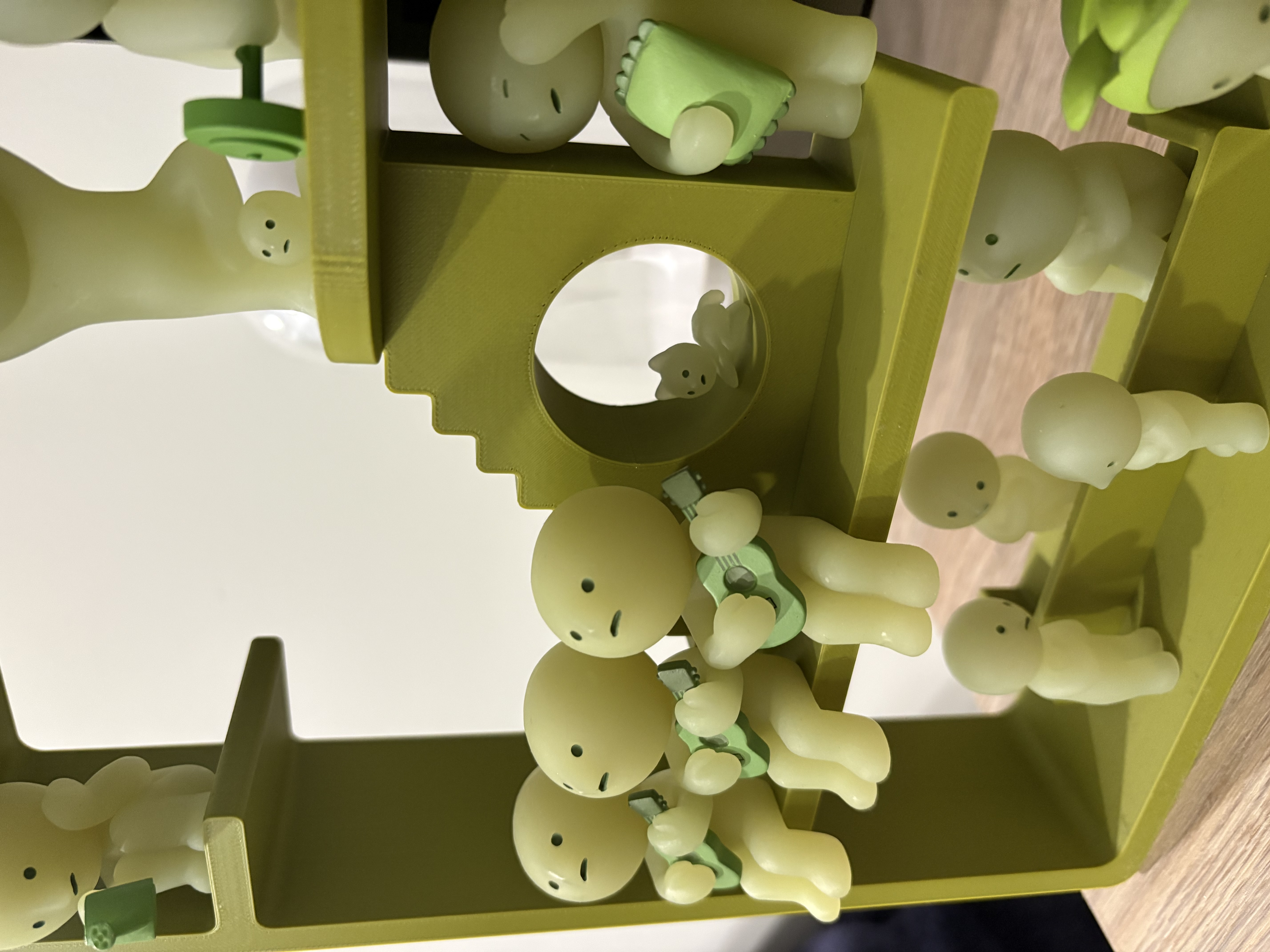 Close-up image of the second layer of the 3D printed green house with smiski figurines positioned on it. There are three figurines holding guitars sitting on the second floor, and a sleepy figure with a pillow standing behind them.