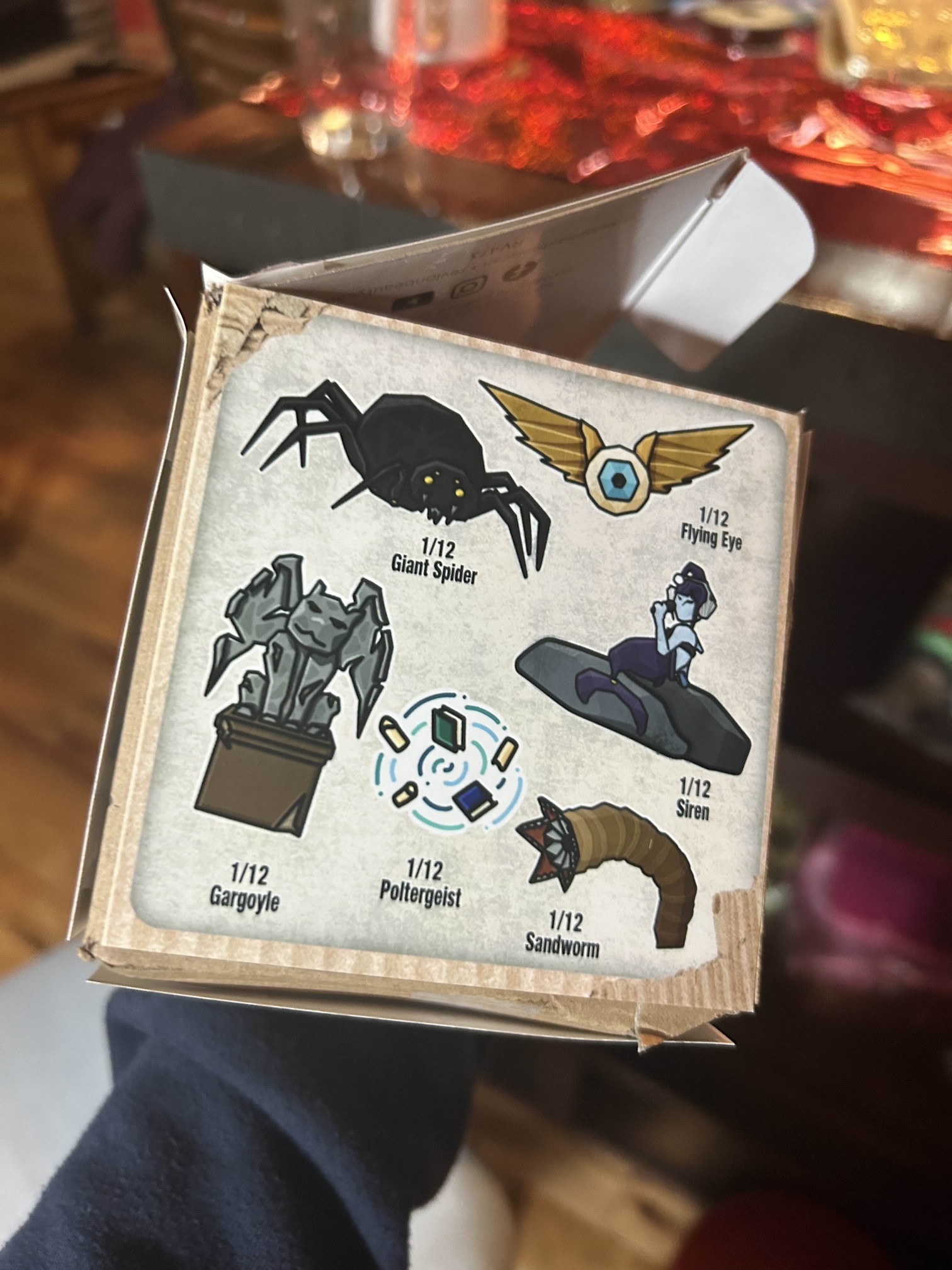 An illustrated cardboard box with a series of possible "collectible" figurines - a spider, flying eye, siren, gargoyle, sandworm, and a polergeist.
