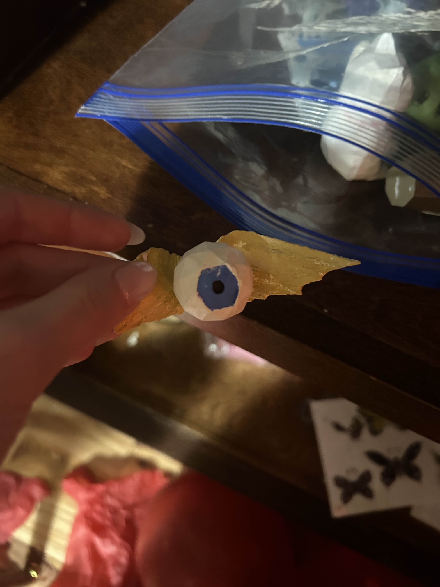 A small 3D printed figurine of a flying eyeball. The wings are gold, and the eye is white with a blue iris.