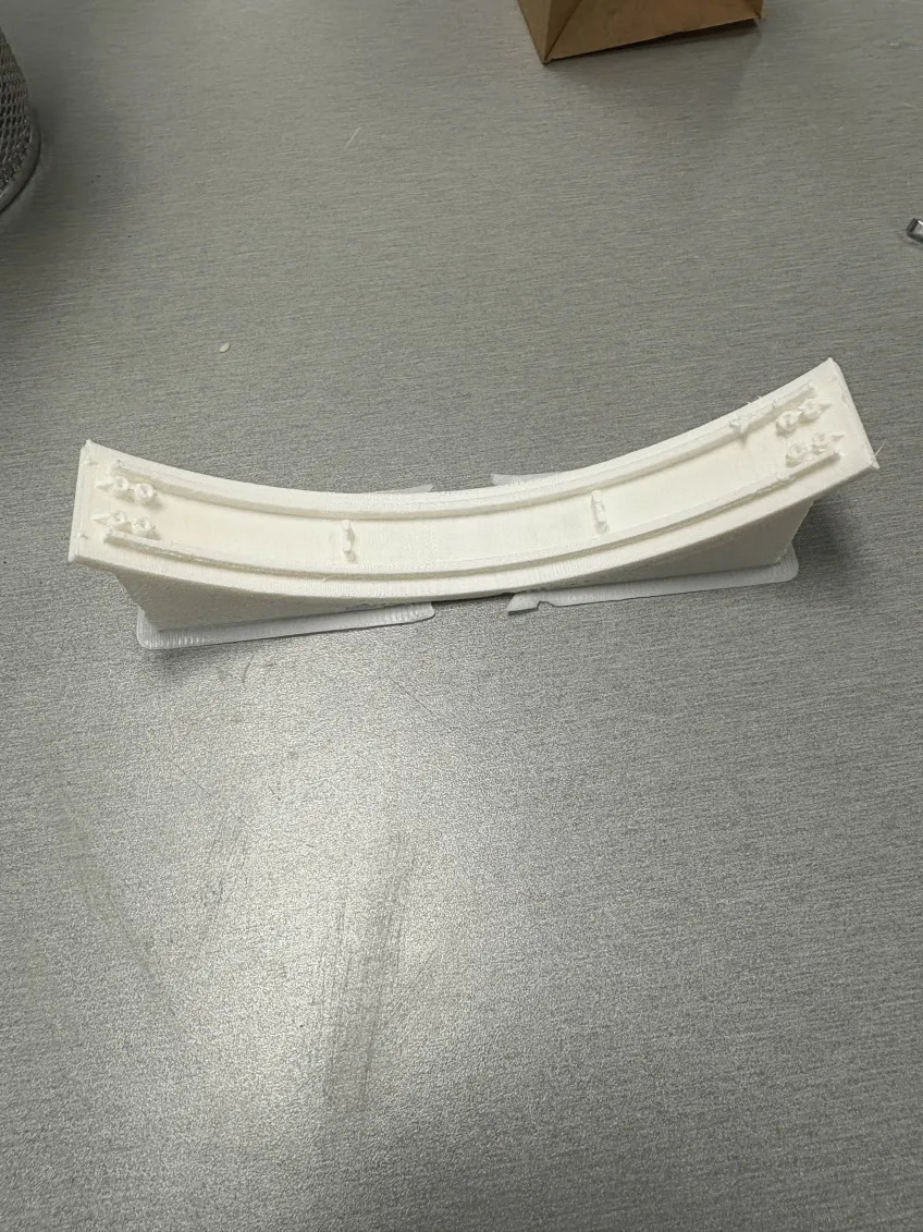 White 3D printed headband for a pair of headphones, with the supports still attached underneath.