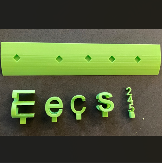 A 3D printed lime green baseplate and 3d standing letters/numbers laying down on a black table. The standing letters show different words, depending on how you look at them - from this angle, it reads "EECS 245".