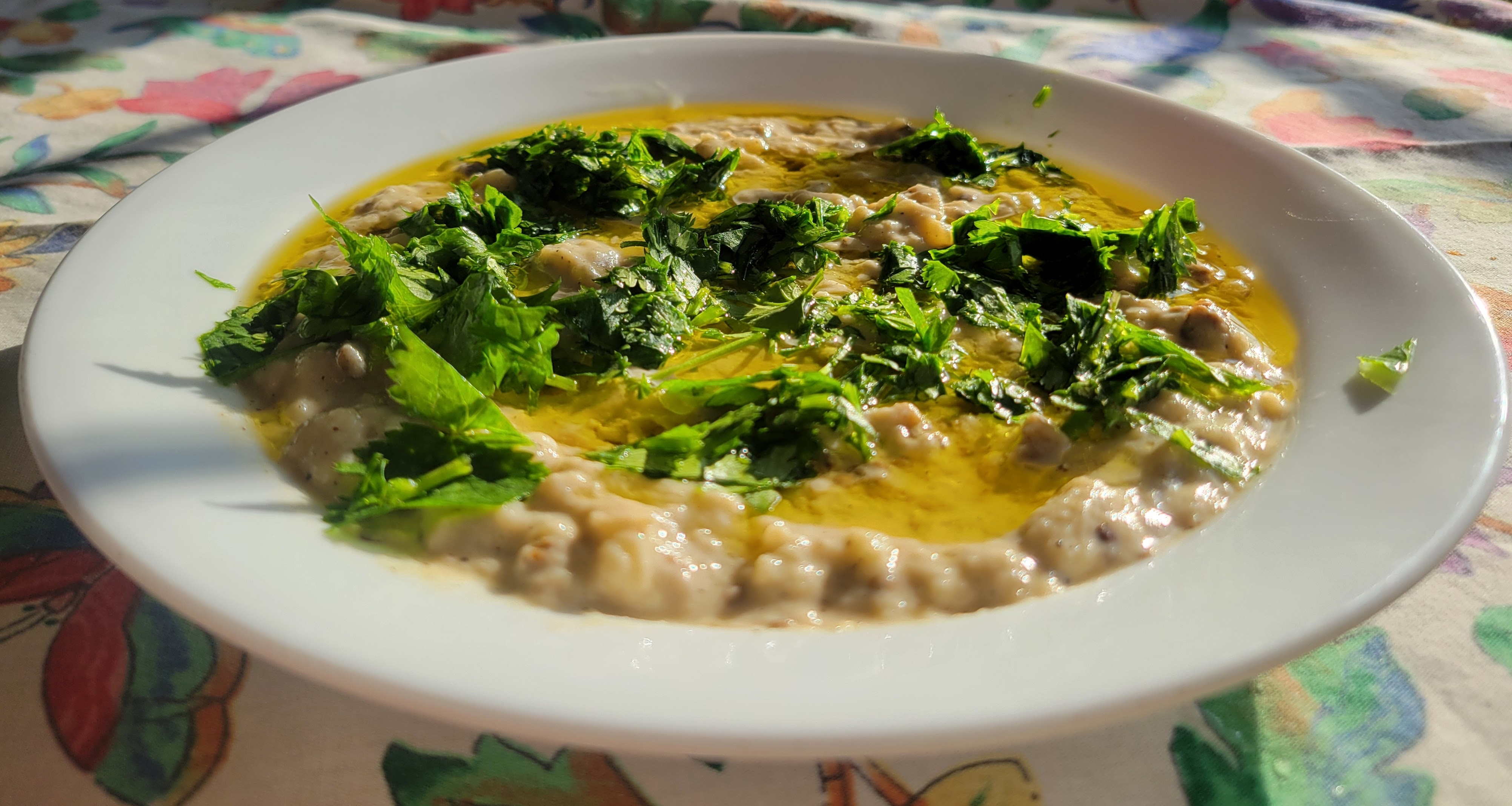 A bowl of tan baba ghanoush, drizzled with olive oil and sprinkled with cilantro