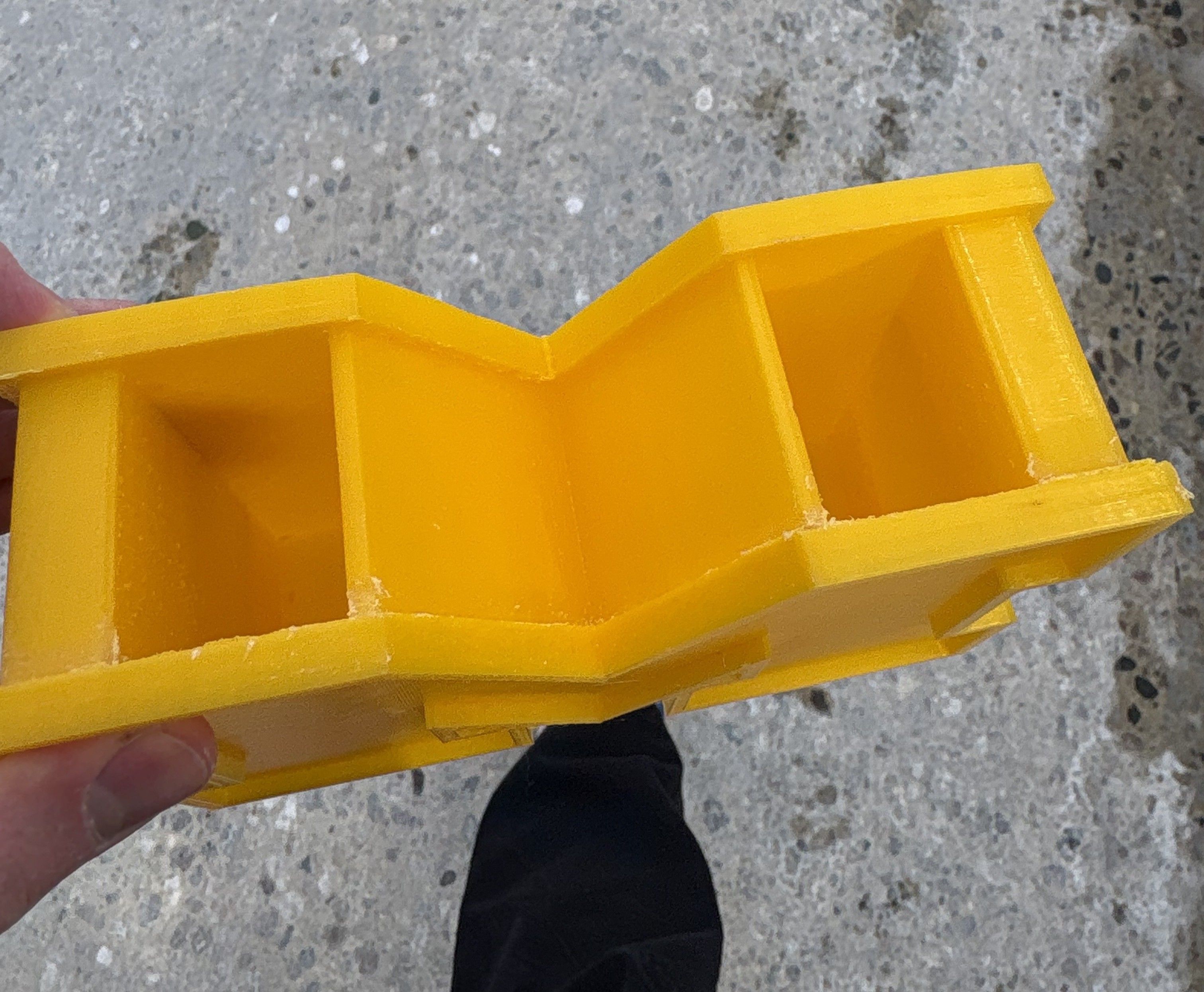3D printed yellow pencil case in the style of the UMich block M. This angle is showing the top of the case, where there are two holes on top of the "M" to store pencils. 