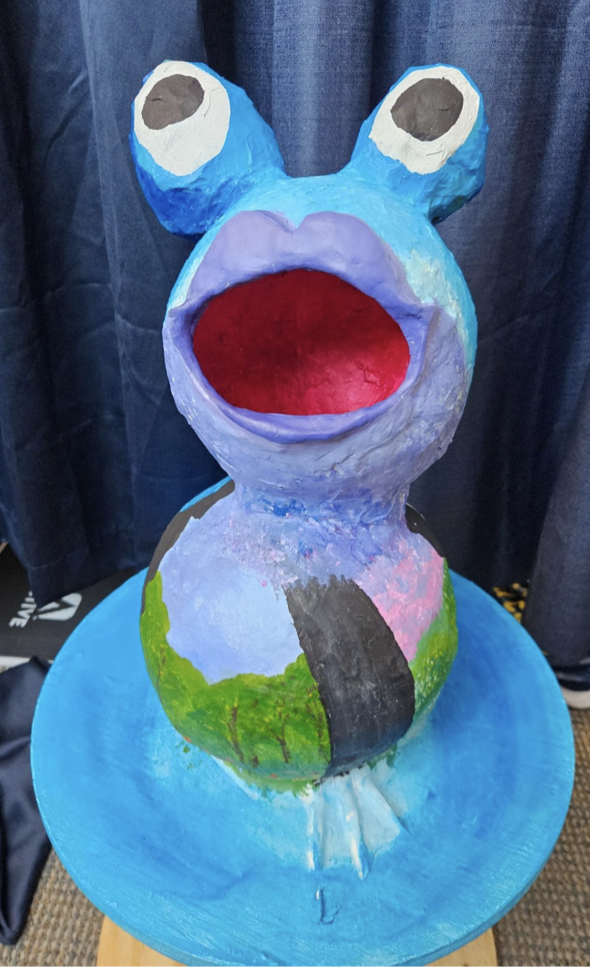 Open-mouthed paper mache frog decorated with images of the four seasons, one on each side. Should we have a naming contest for this frog?