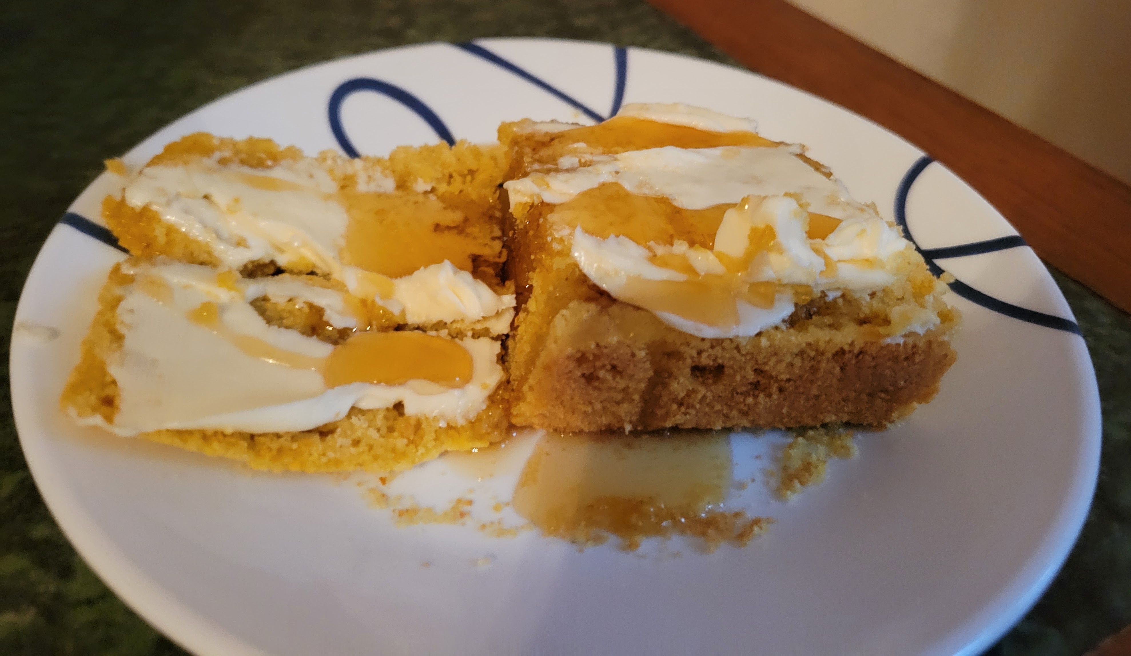 A slice of cornbread on a white plate. It has been split in half and slathered with margarine and maple syrup