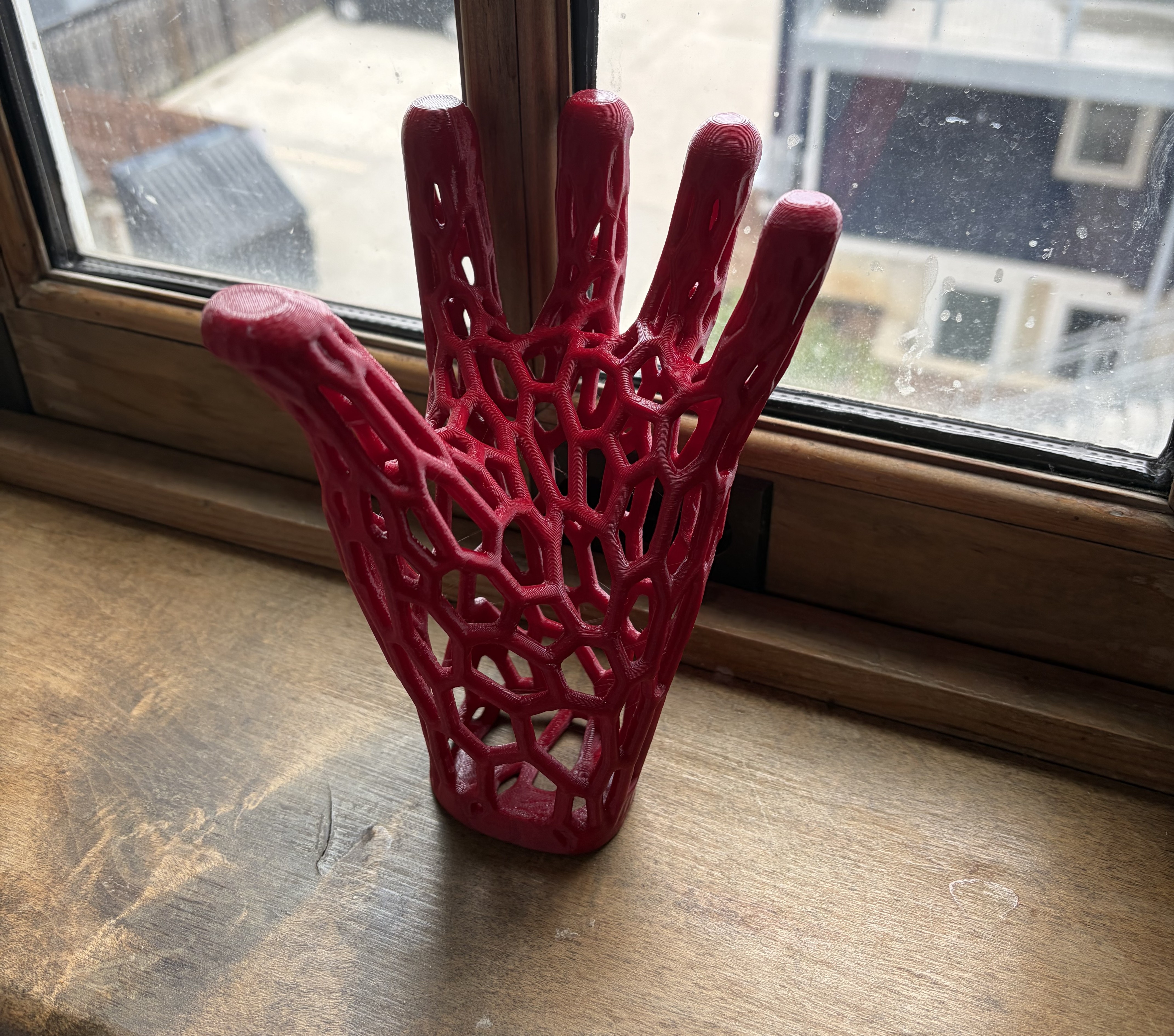A 3D printed red webbed hand, placed upright on its wrist on a wooden windowsill.
