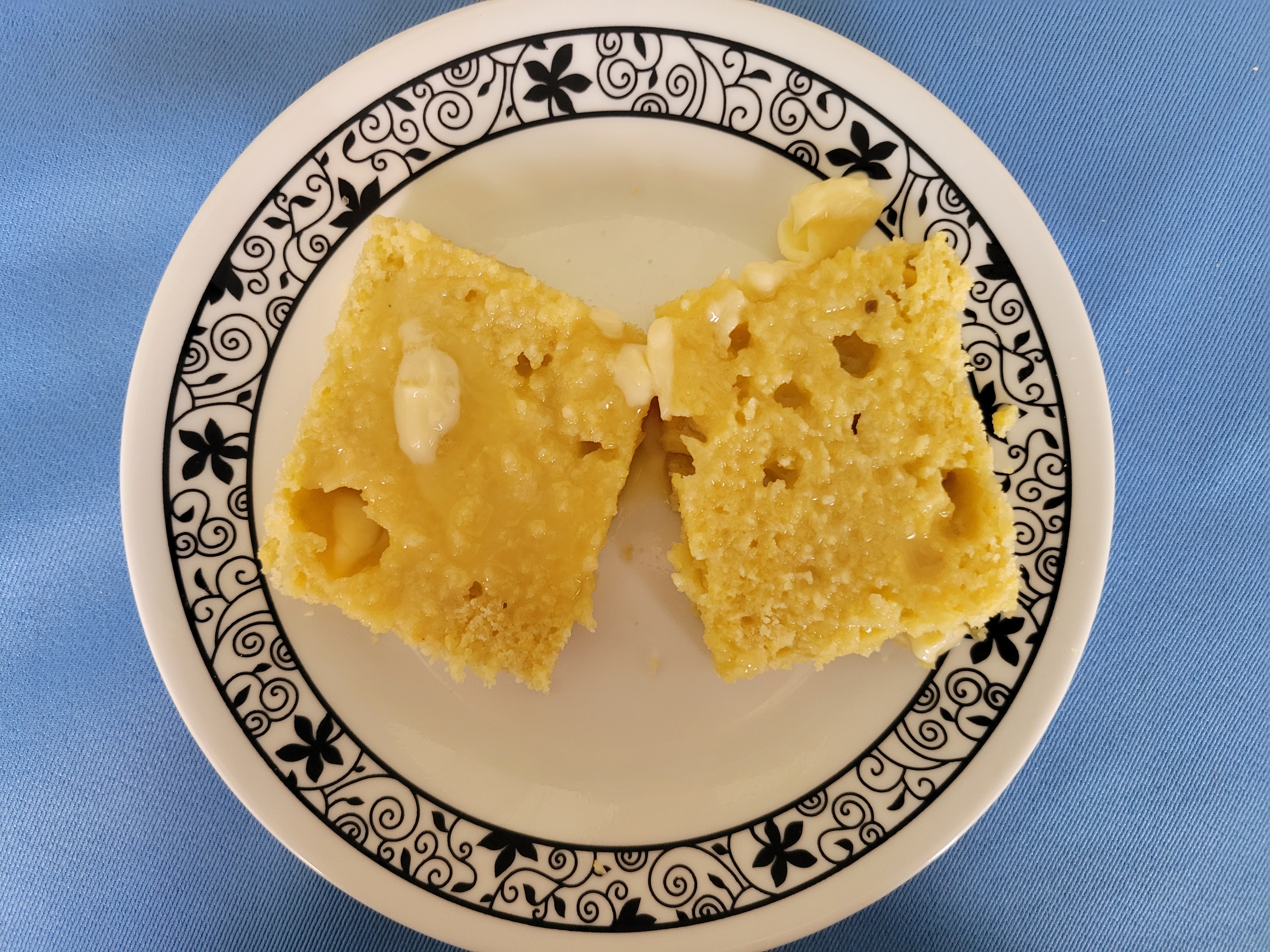 Cornbread split in half, with margarine melted into it. Large air bubbles are visible in the bread. 