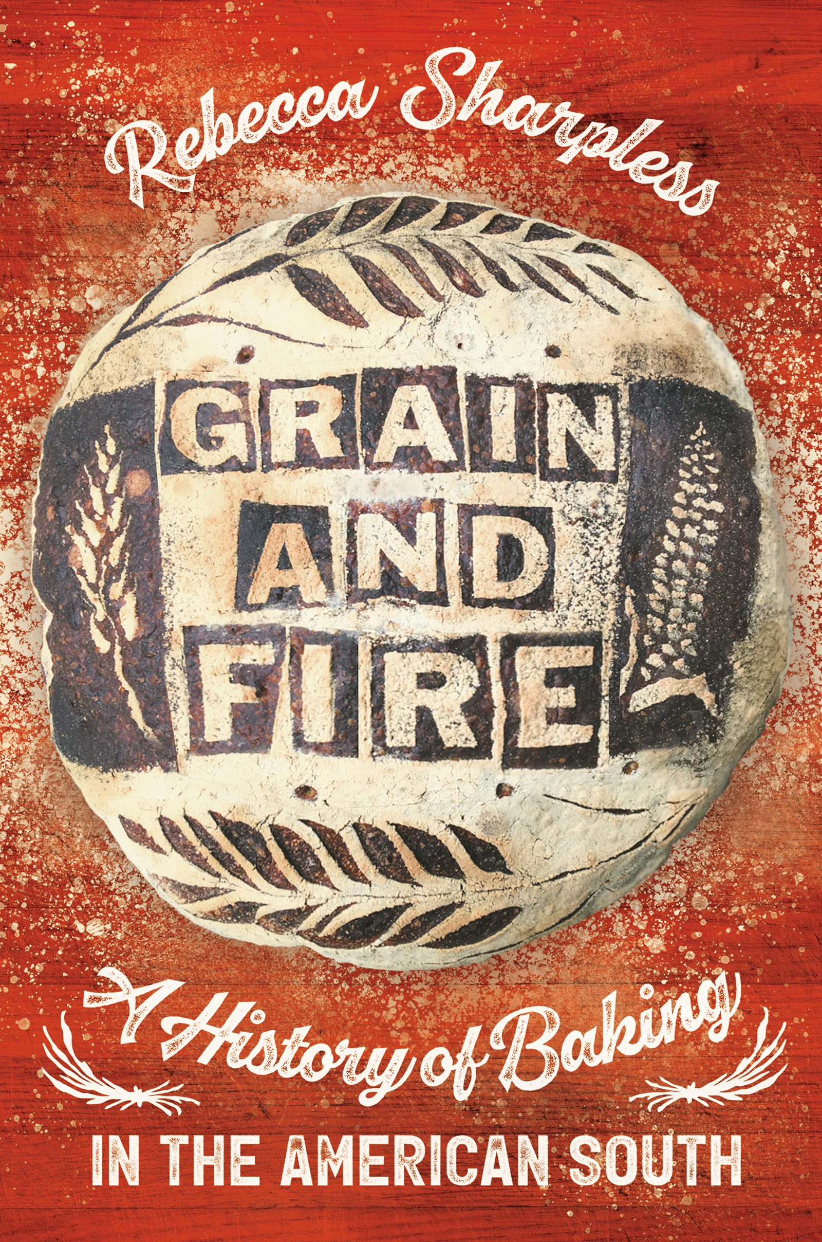 Red book cover with the title Grain and Fire appearing outlined in black (like scorched bread) on an illustration of a loaf decorated with a wheat shef and corn cob