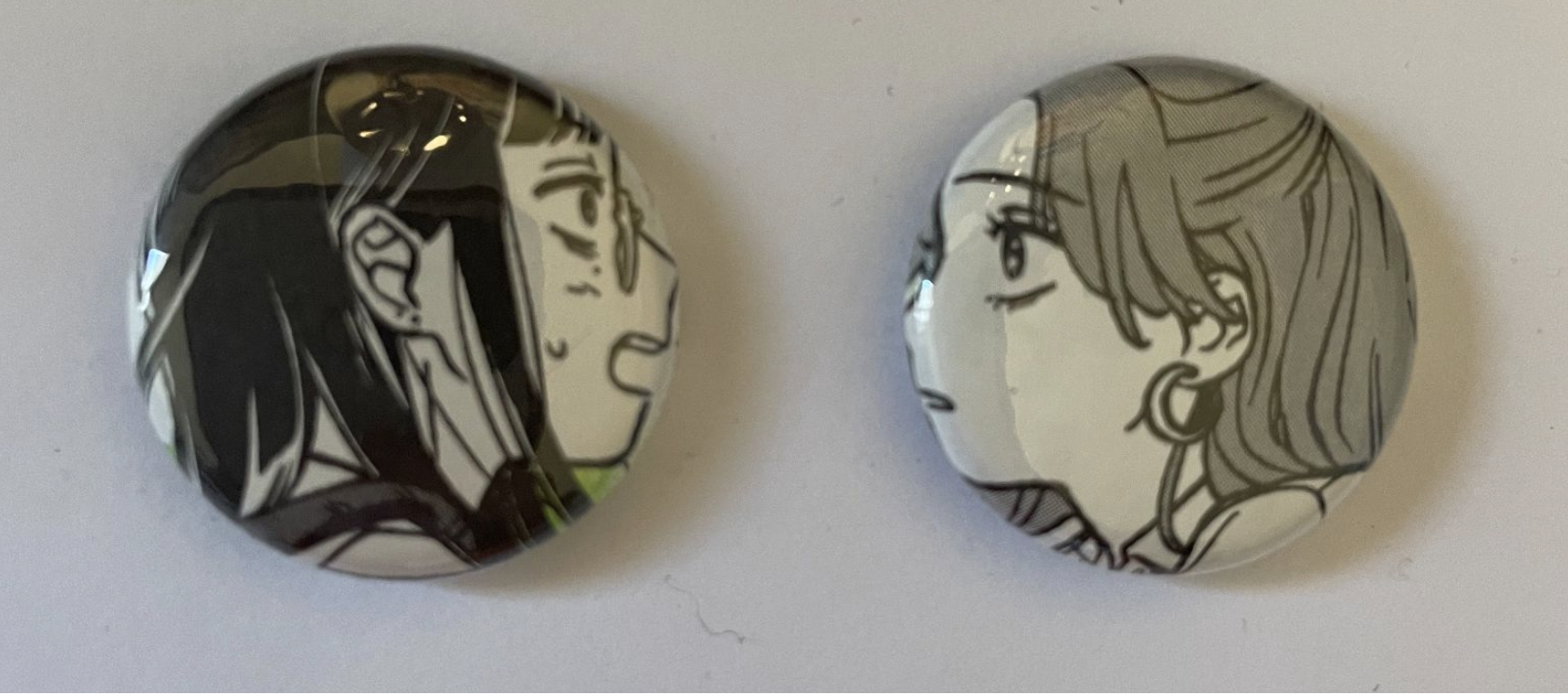 Two black-and-white buttons with the faces of a girl with black hair looking at a girl with brown hair