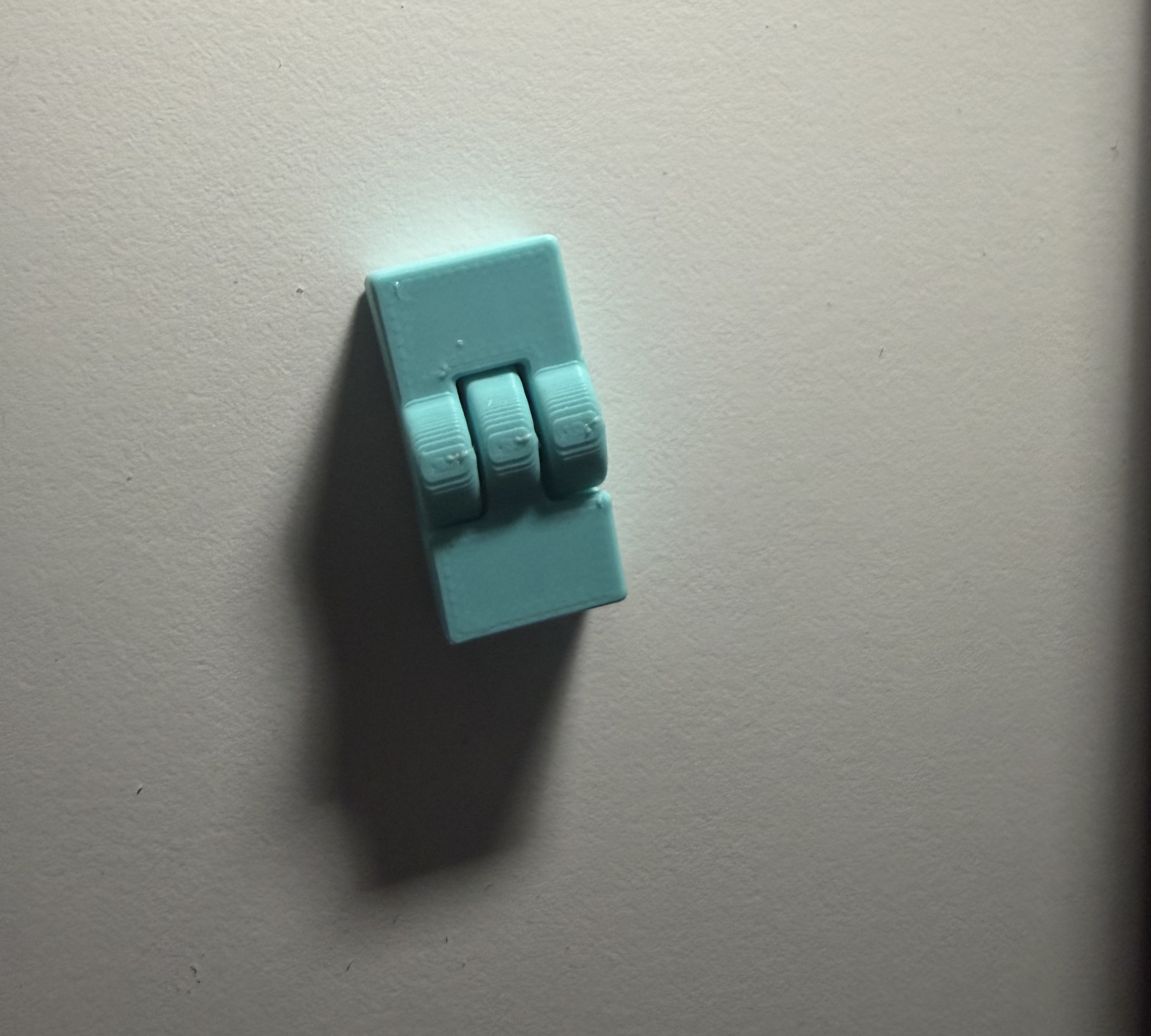 A light blue 3D printed hinge joint on a white table. The hinge is "open", and is laid vertically on the table. In the middle of the joint the connections between the two halves are visible as three vertical lines in the middle third of the print.