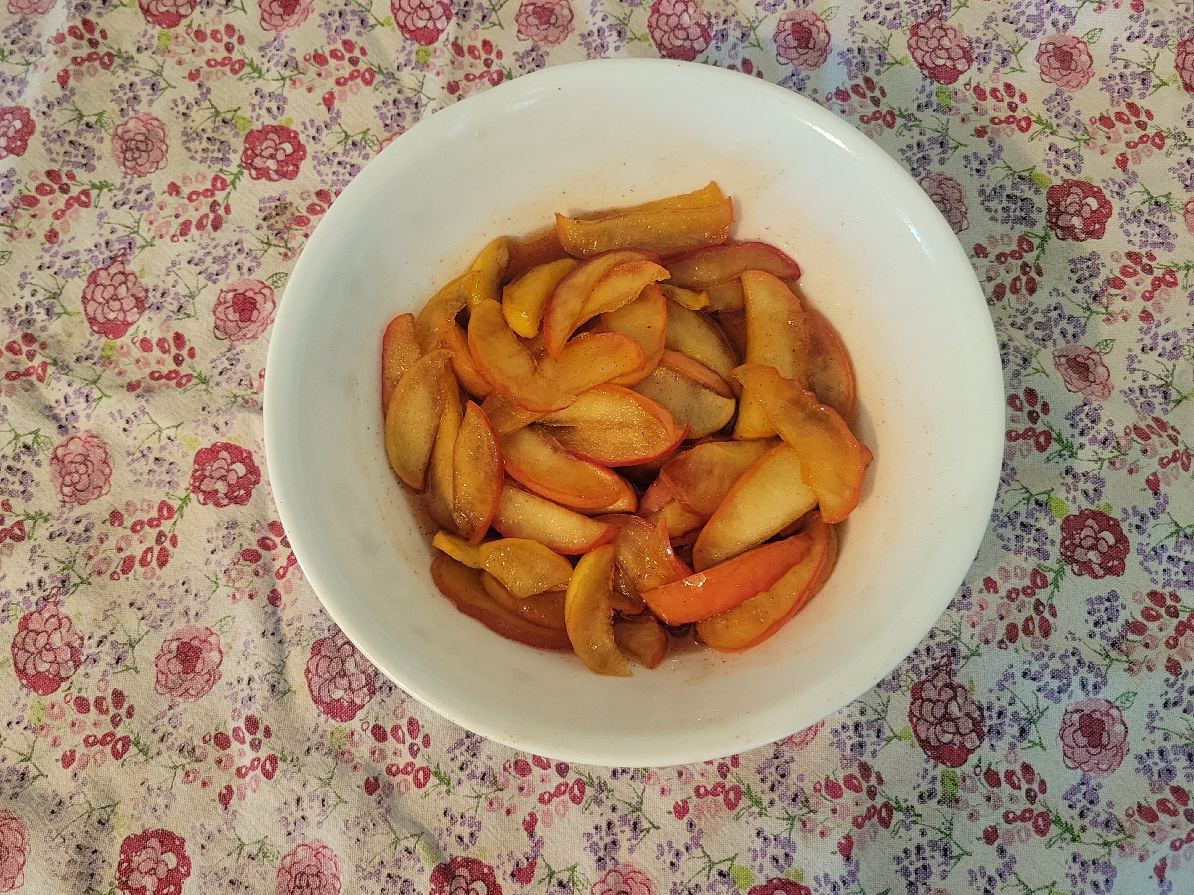 A bowl of sliced, pickled apples on a pink floral tablecloth