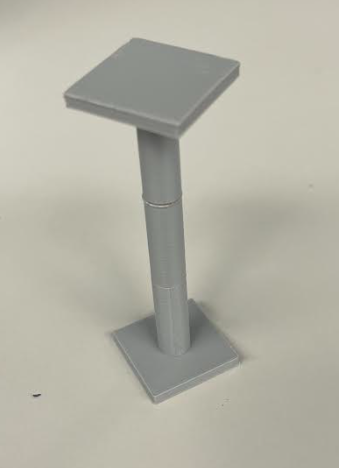 Grey 3D printed pedestal with square base, top, and a cylindrical middle piece positioned upright on a white surface.
