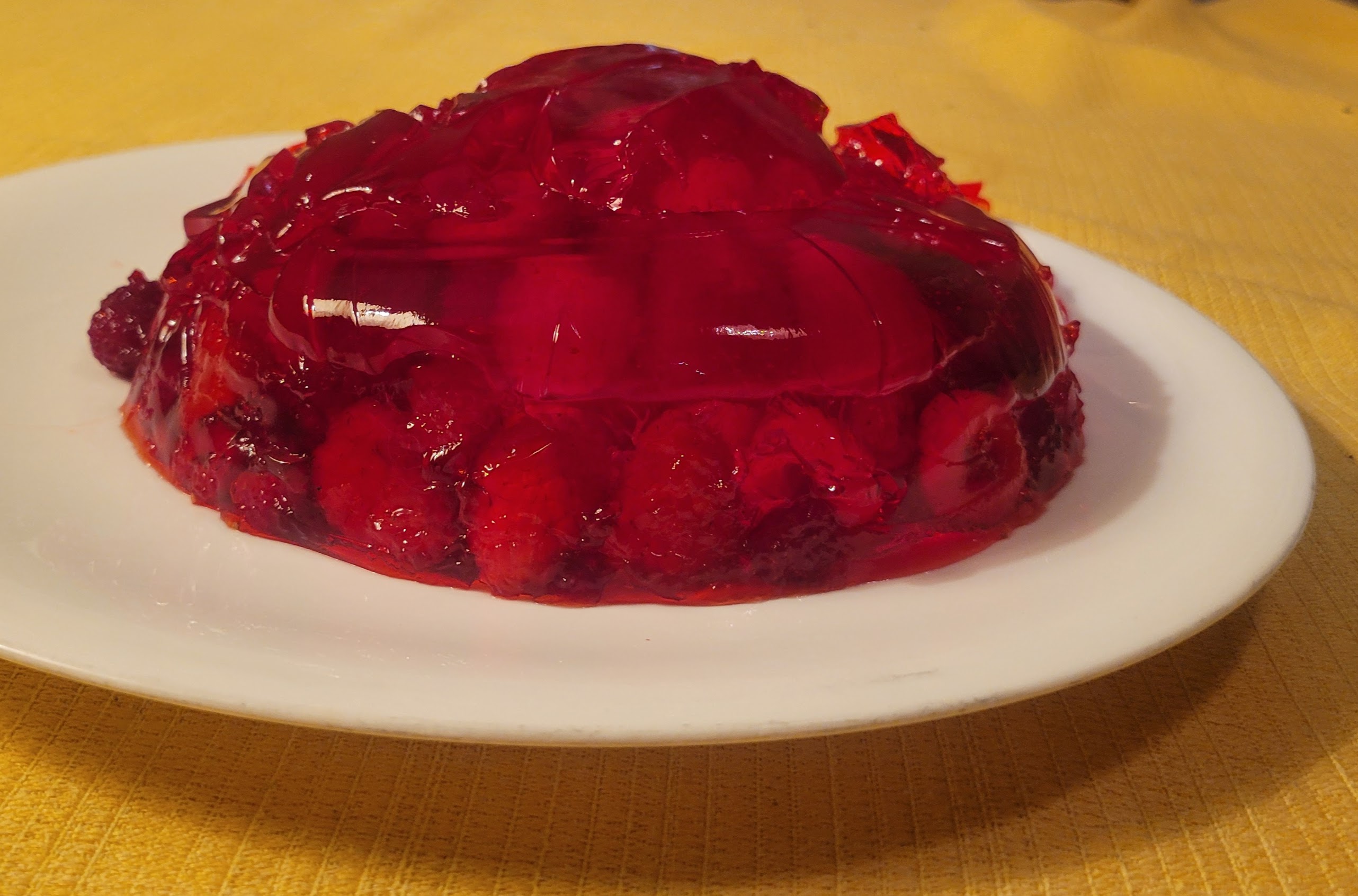 A mound of red jell-o on a white plate. Raspberries are visible through the translucent gelatin dessert