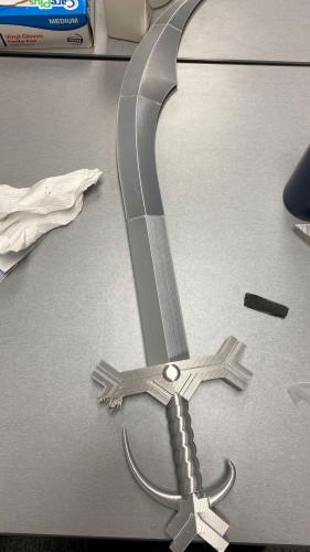 3D printed silver simitar sword lying on a table after sanding and fitting the multiples pieces together