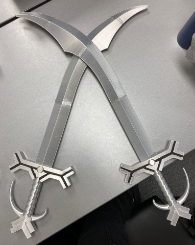two silver 3D printed simitar swords lying across one another on table