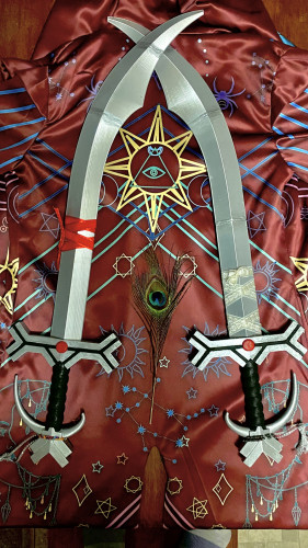 two silver 3D printed cosplay simitar swords lying crossed on a red celestial printed fabric with a peacock feather between their hilts