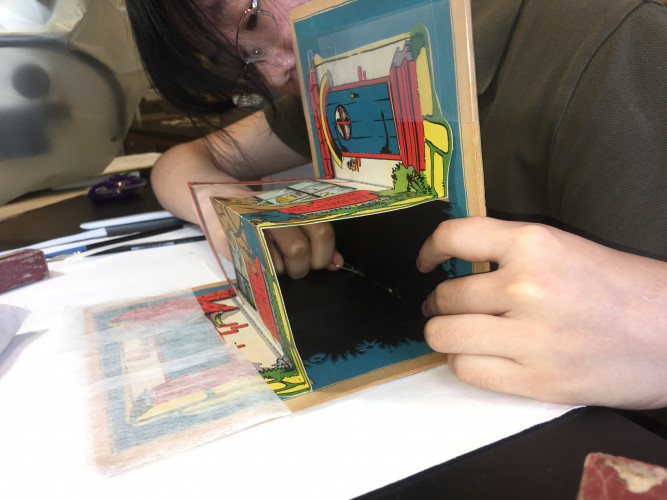 image of a person reaching hands through the book to stitch in a new spine piece