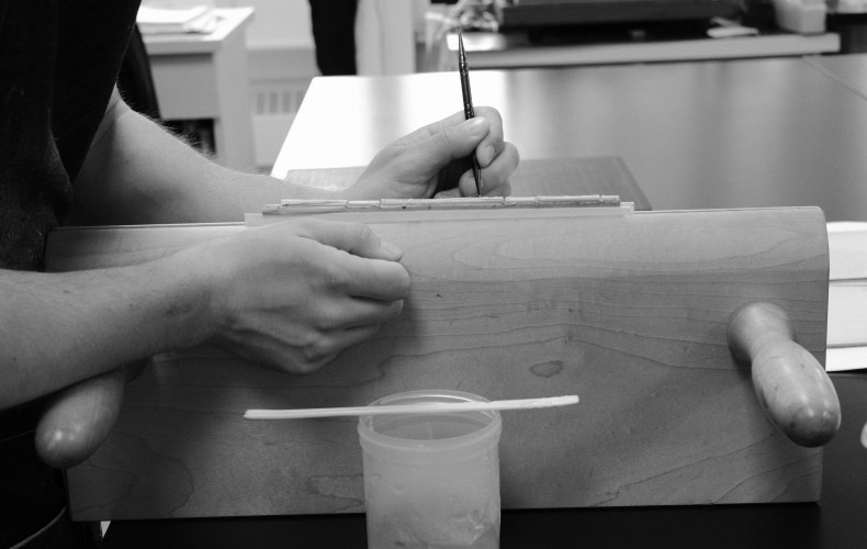 hands holding tools working on the spine of a book in a press