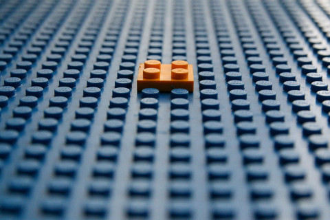 One orange lego in the middle of a blue lego base.